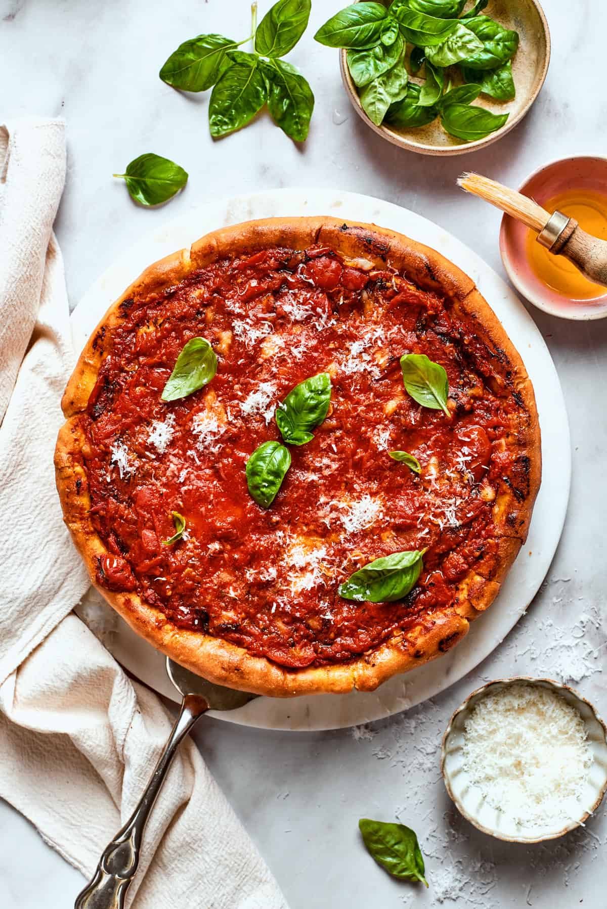 Overhead image of pizza topped with tomato sauce and garnished with fresh basil leaves.