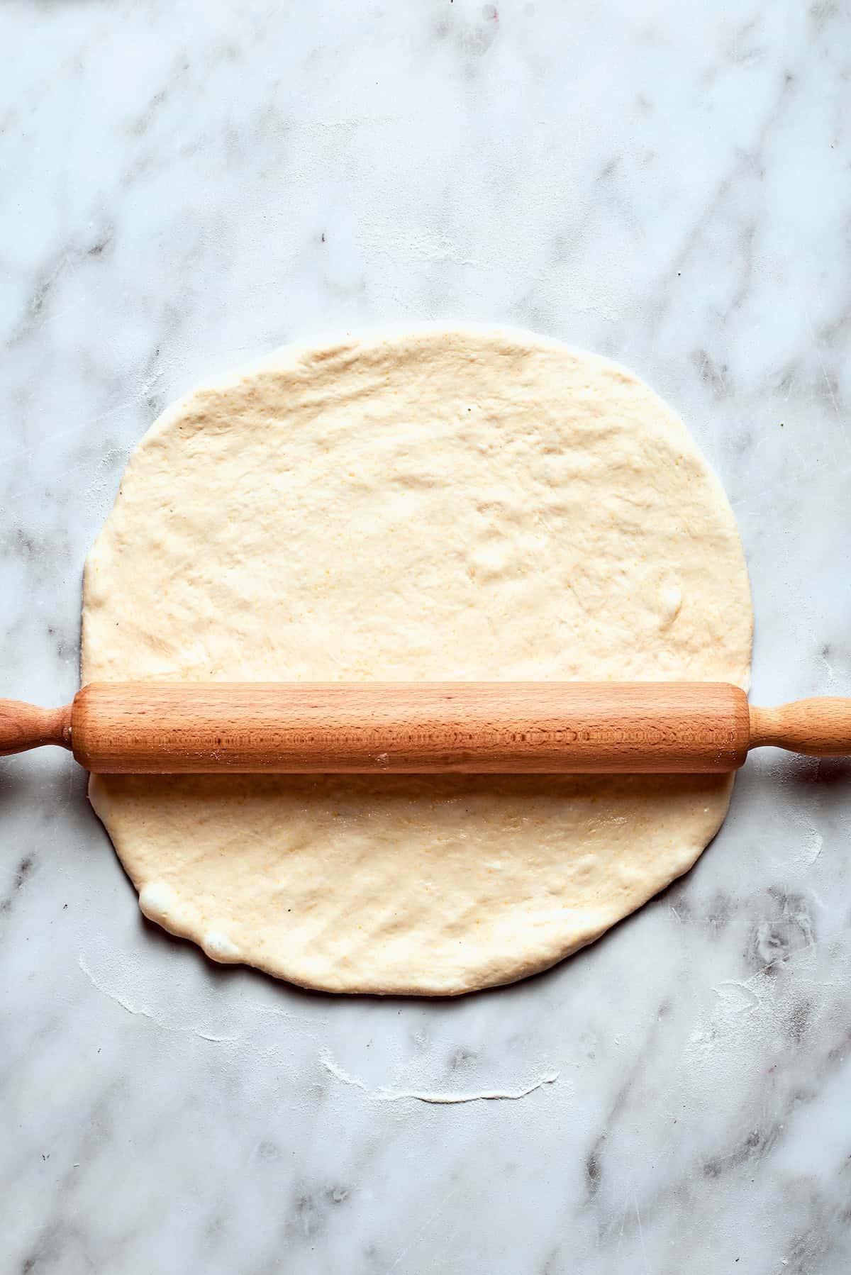 A rolling pin rolls out the pizza dough.