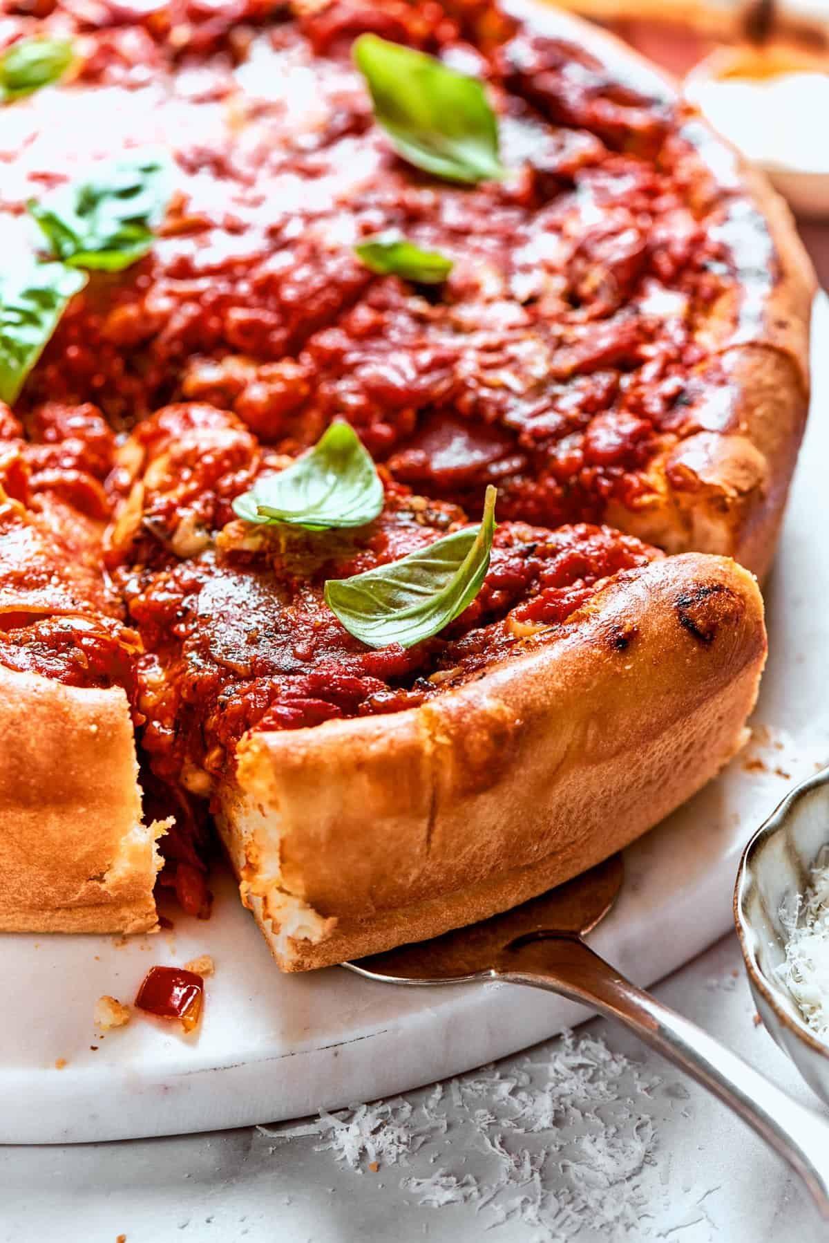 Serving spoon lifting out a slice of deep dish pizza.