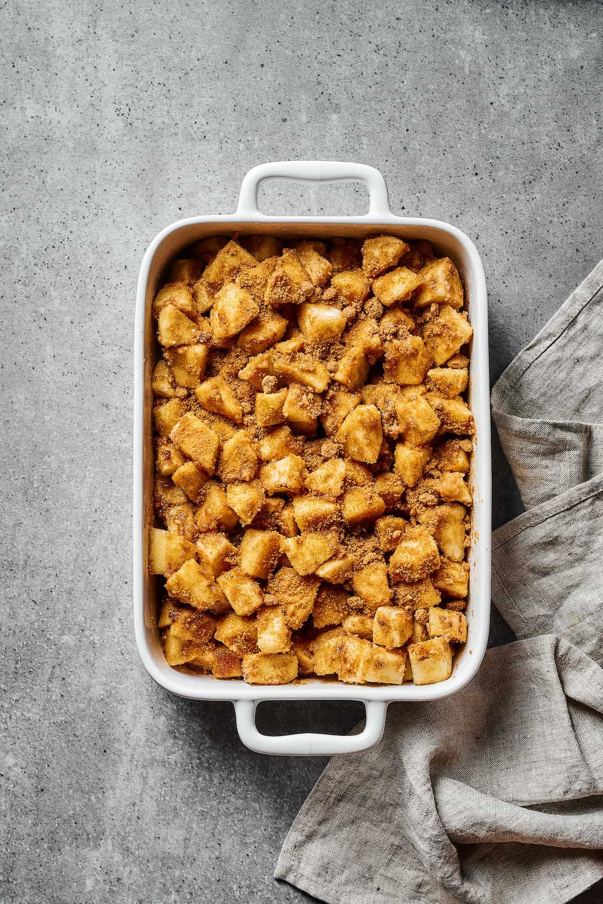 Apples coated in a spiced flour mixture, in a large baking dish.