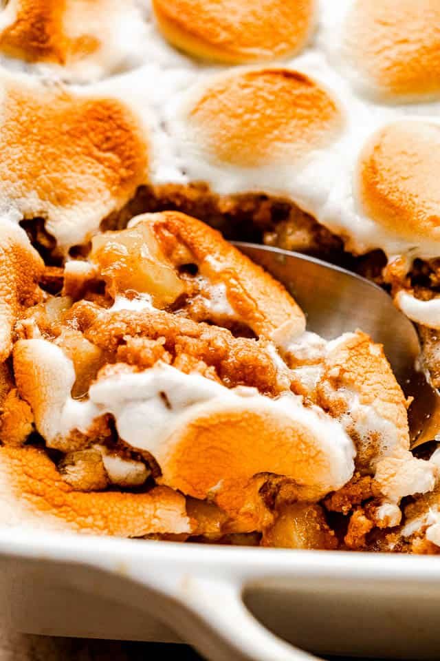 cutting into marshmallow topped apple crumble with a serving spoon