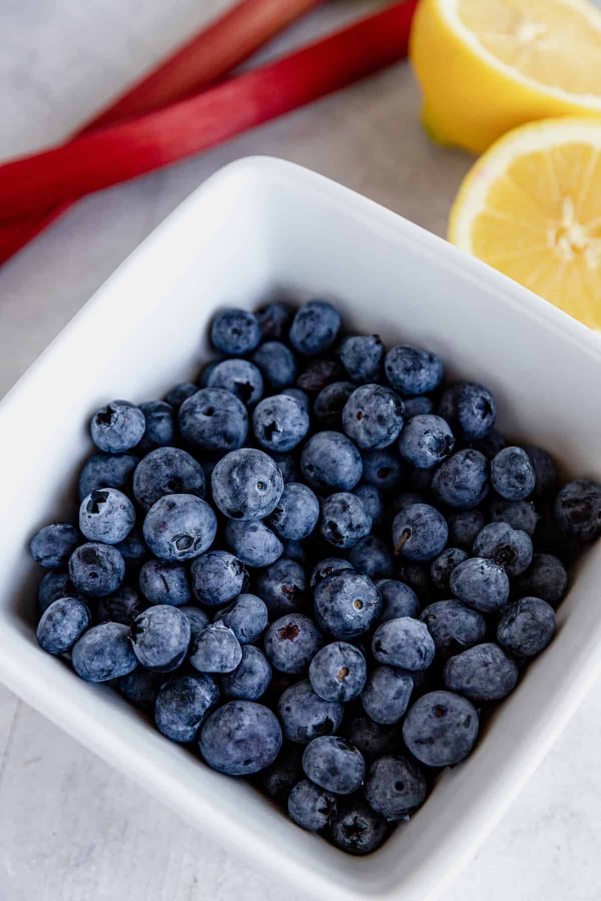 A Bowl of Blueberries Beside Rhubarb and a Fresh Lemon Cut in Half