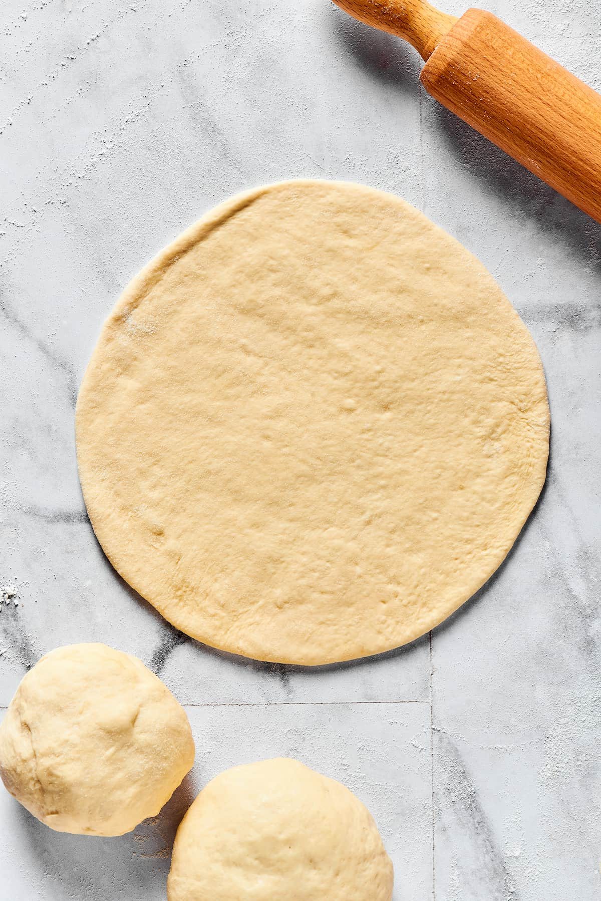 Dough rolled into a thin circle on a floured work surface.