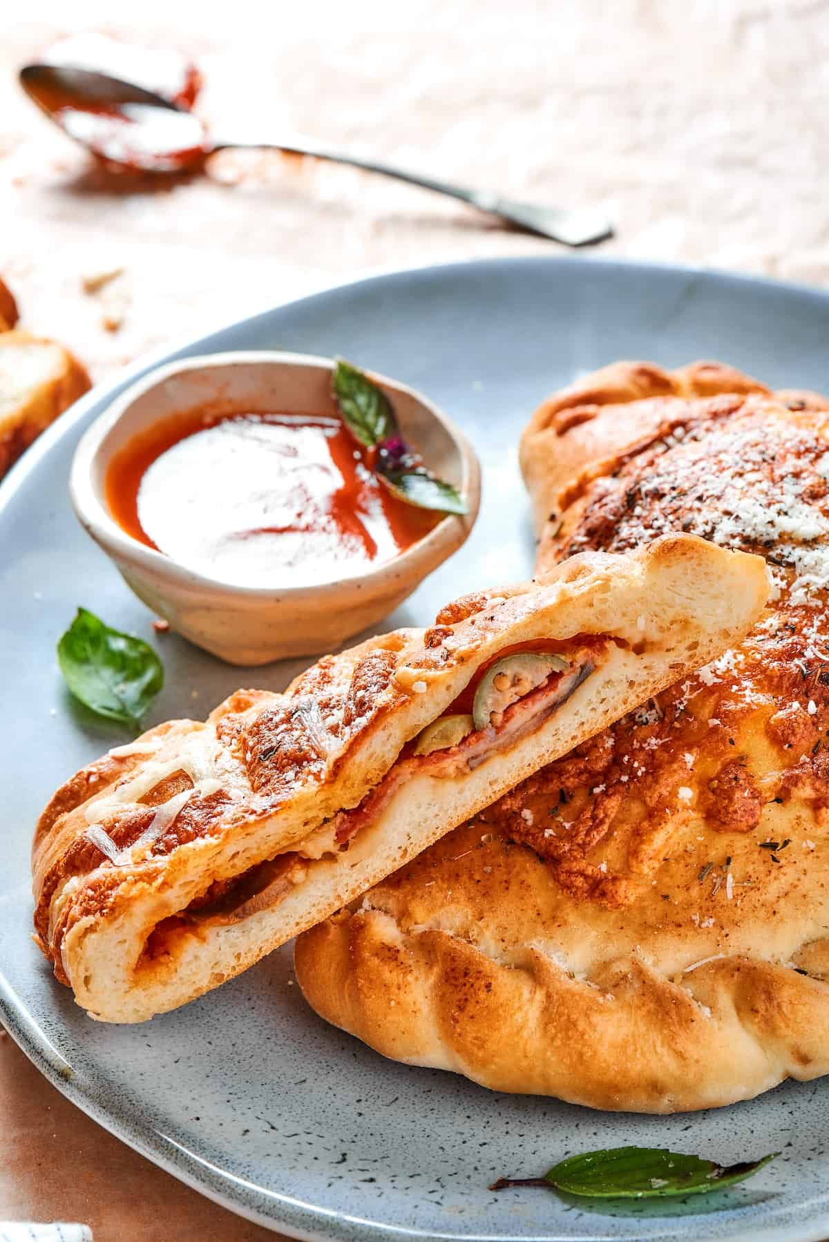 A cut pizza pocket on a blue plate with dipping sauce.
