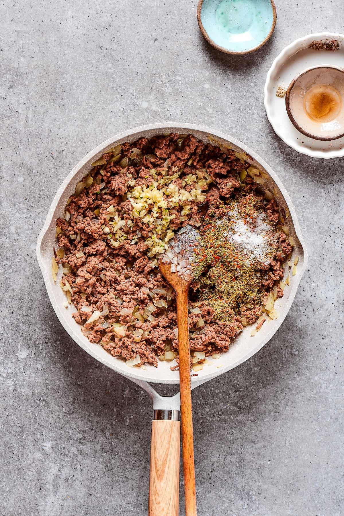 Adding seasonings to a skillet of beef and onions.