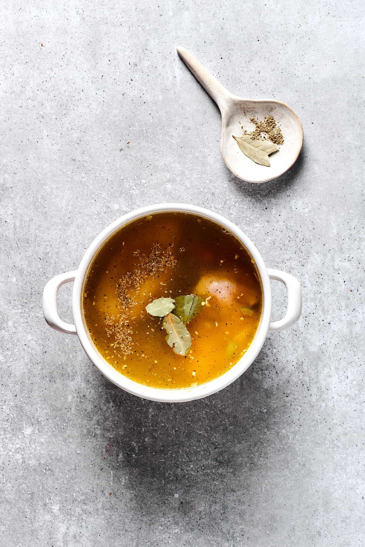 Broth and herbs added to a soup pot.