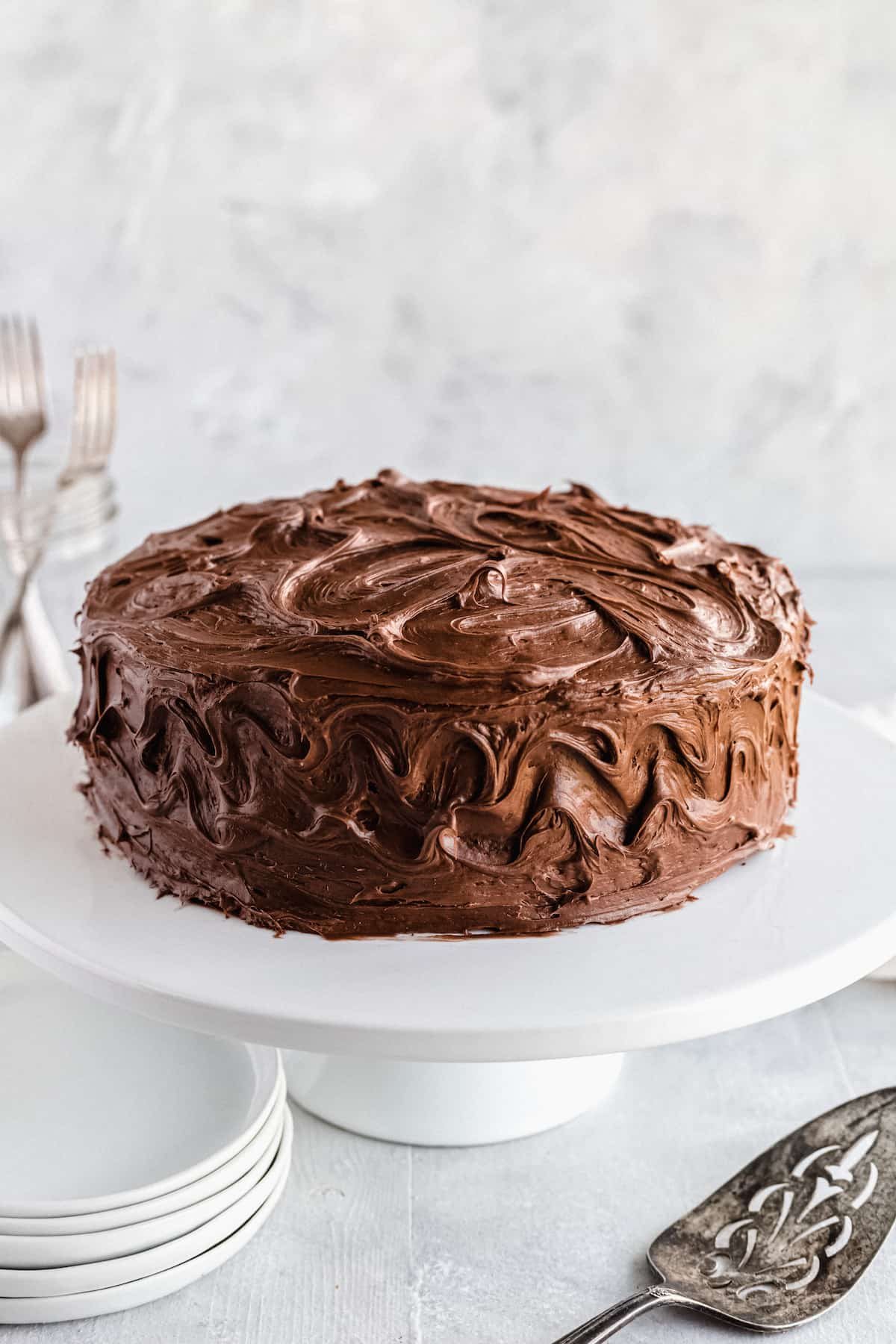 A Frosted Chocolate Cake on a White Stand with a Dessert Spatula in the Foreground