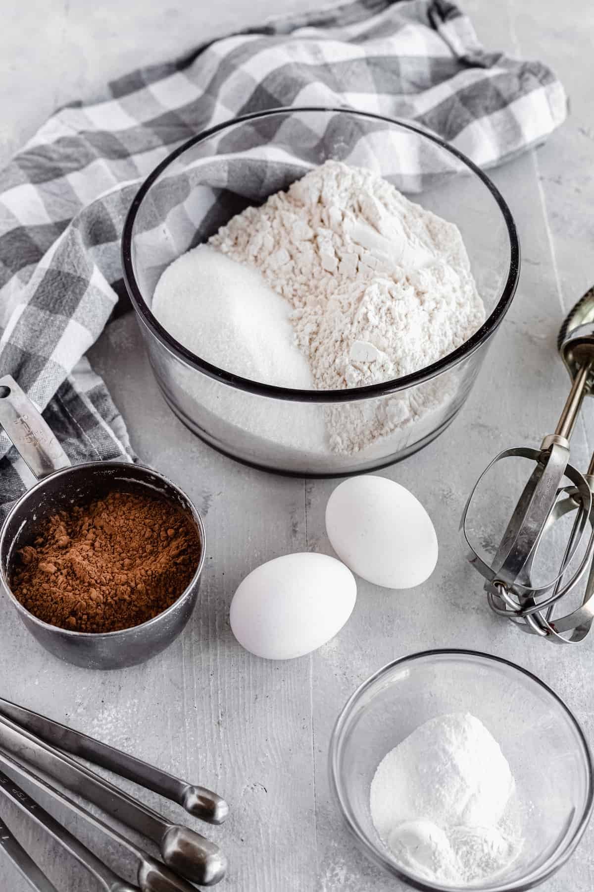 Cocoa Powder, Eggs, Baking Soda, Baking Powder and the Rest of the Cake Ingredients Arranged on a Gray Countertop