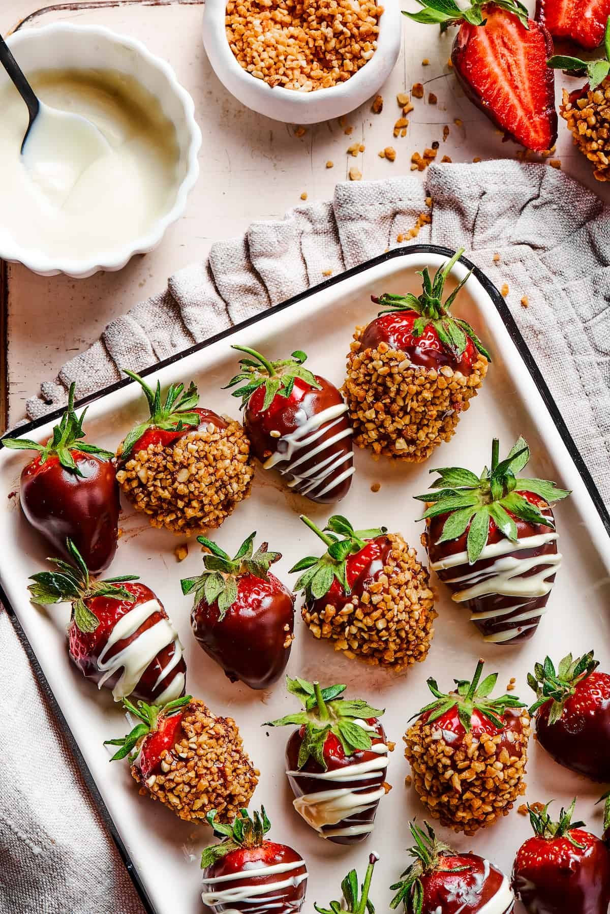 A white tray with a black border, displaying three kinds of chocolate dipped strawberries: plain, white chocolate drizzle, and toasted hazelnuts.