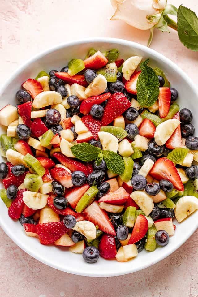 Fresh fruit salad in a large white bowl garnished with fresh mint leaves.