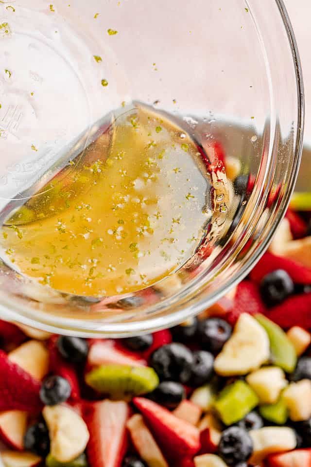 The honey lime dressing being poured on the fruit salad.