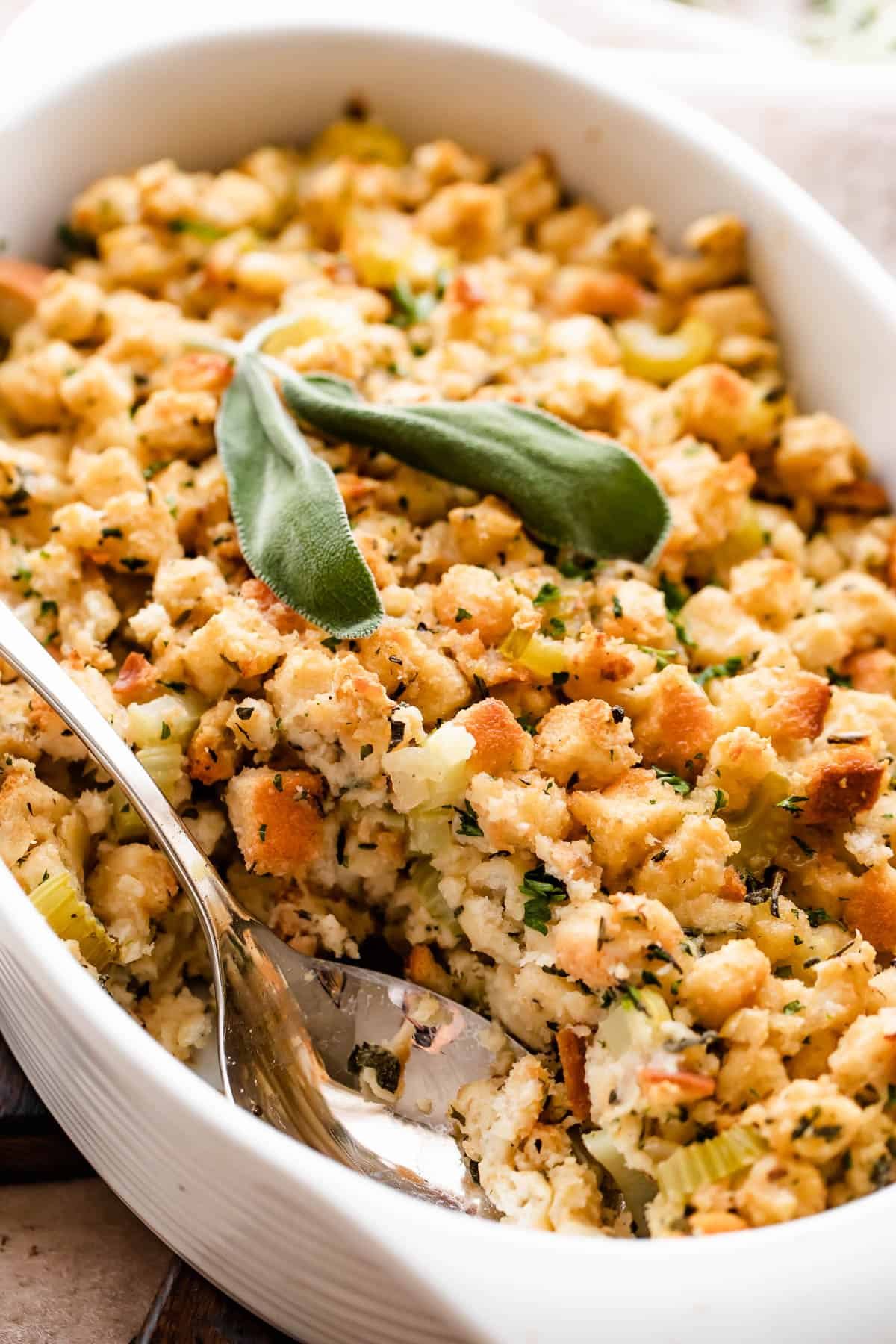 An overhead shot of a scalloped casserole dish, filled with baked bread stuffing. A serving spoon is in the dish.