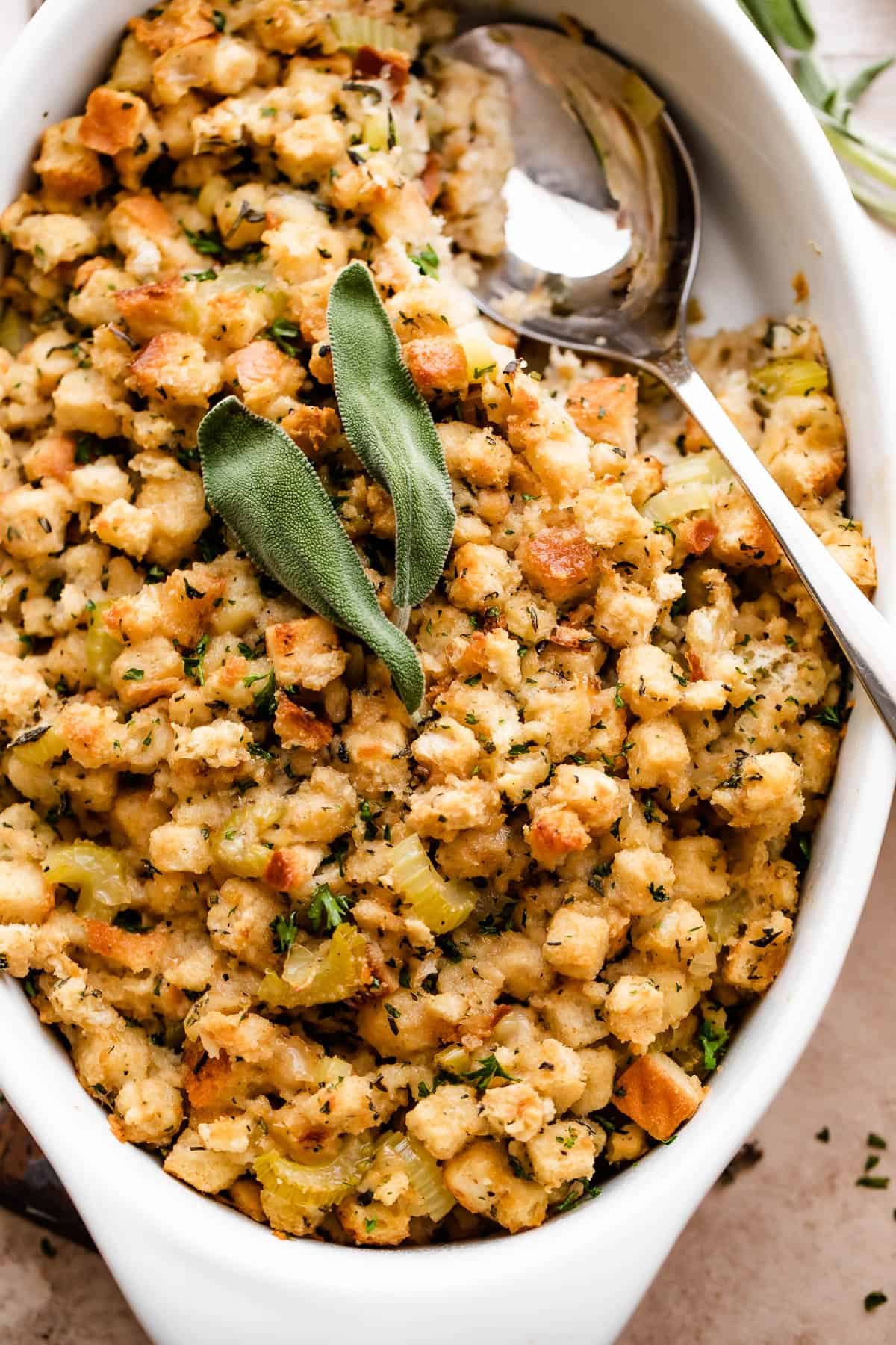 overhead shot of fresh baked stuffing (dressing) sprinkled with sage leaves and herbs in a white dish.