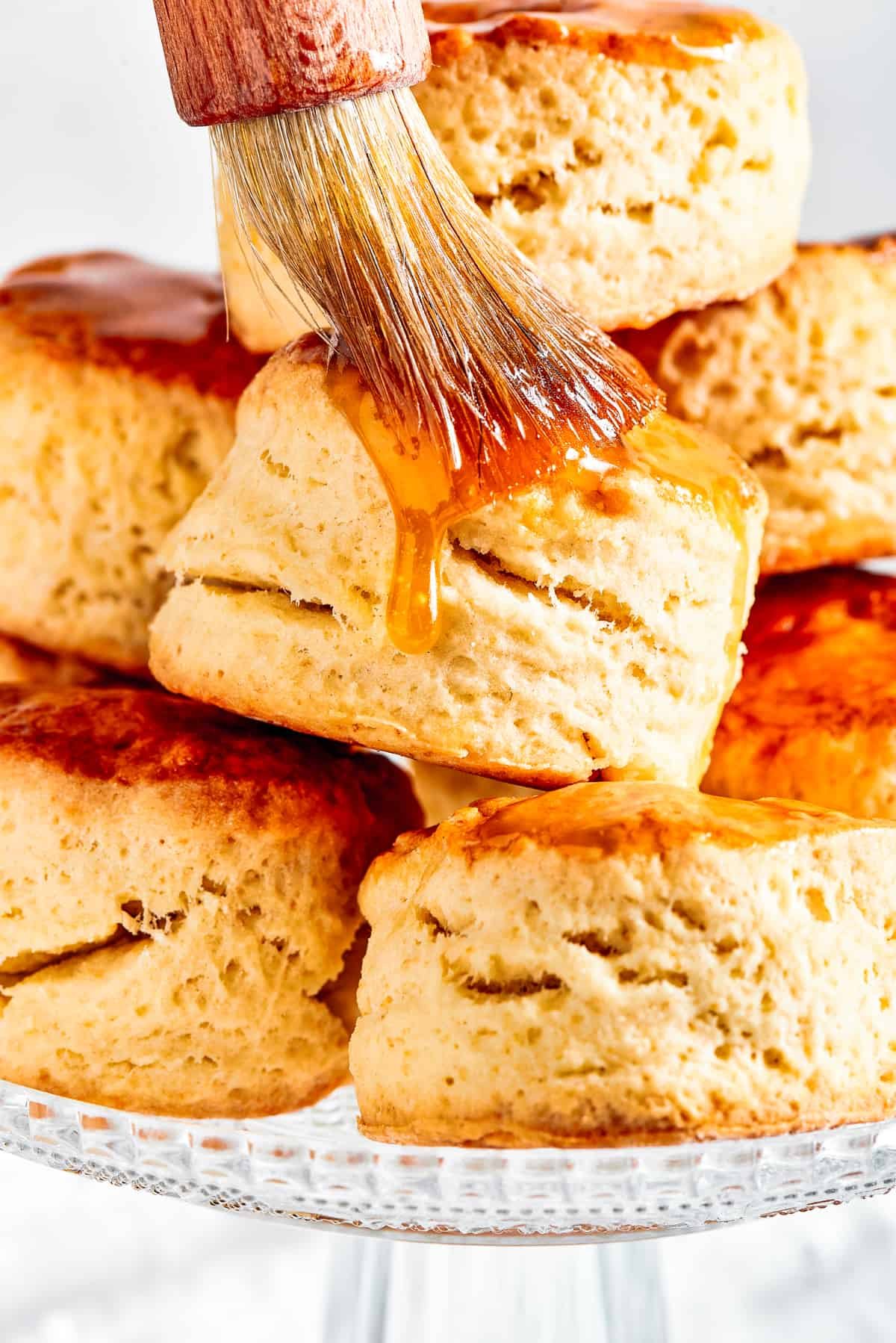 Brushing maple syrup on top of biscuits.