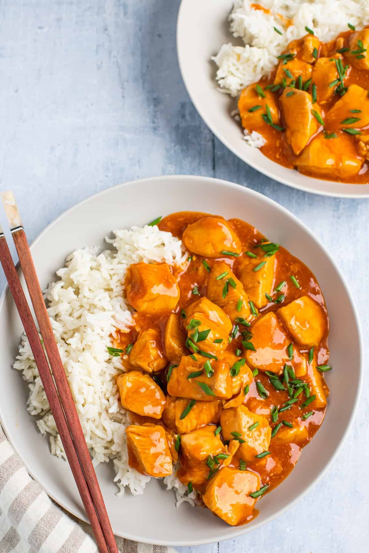 Two plates with servings of orange chicken and rice.