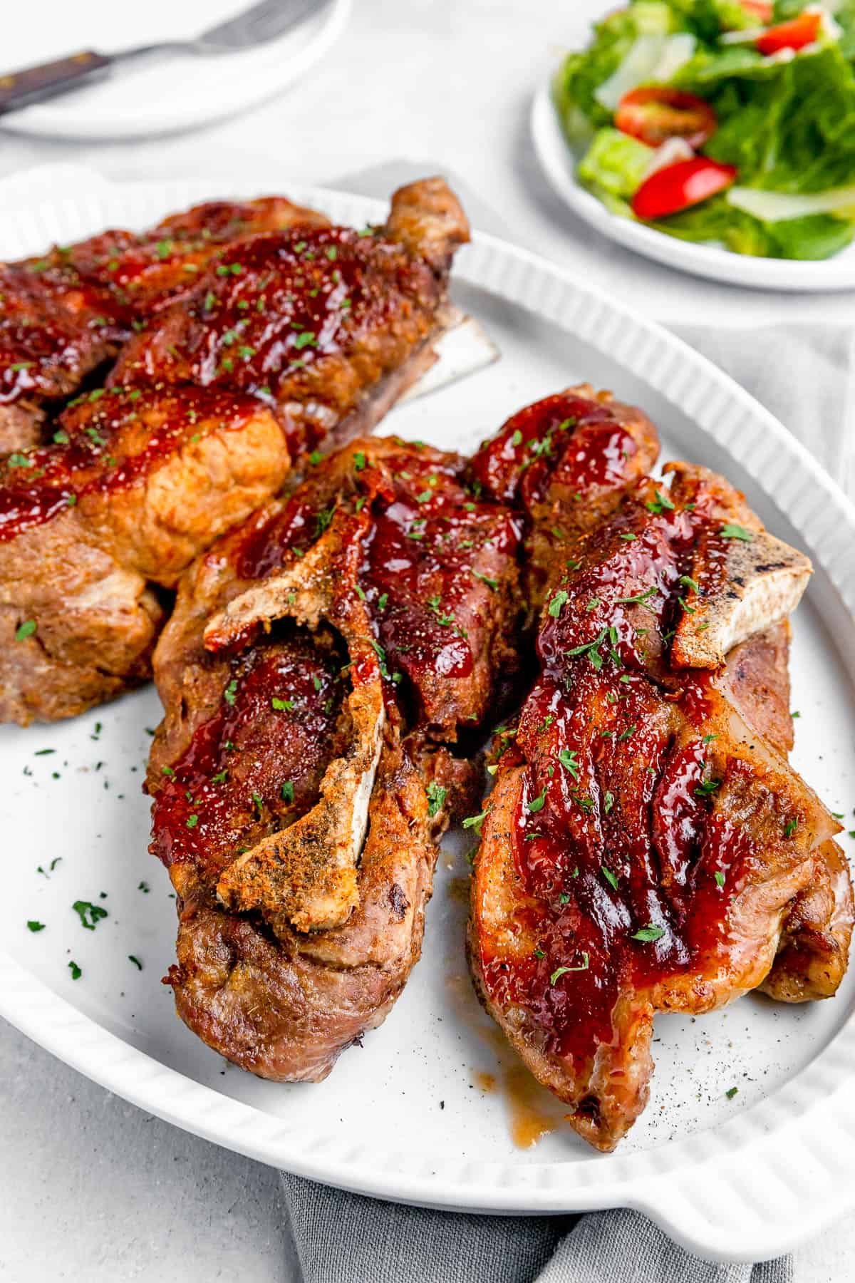 side shot of Instant Pot Ribs on a White Serving Platter with a Small Salad in the Background