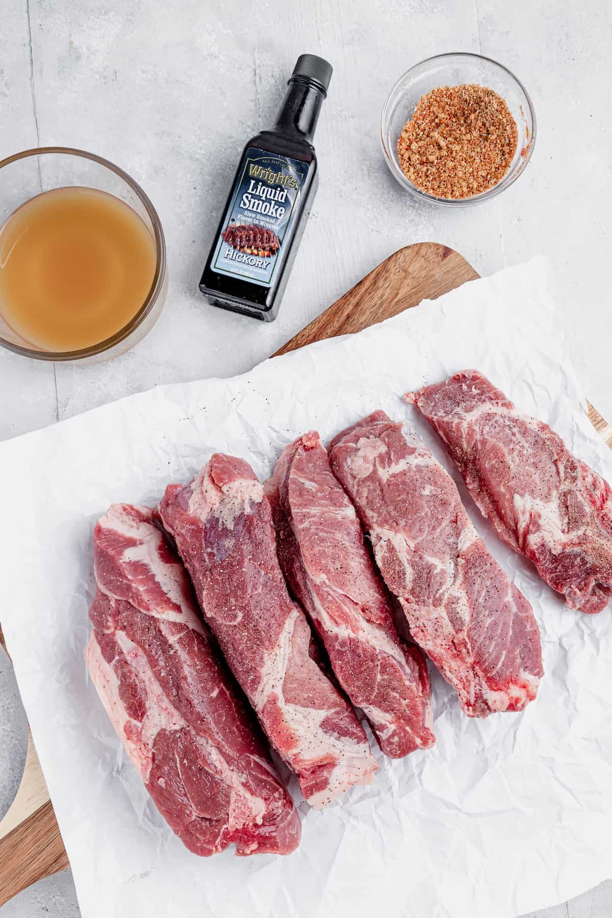 Unccoked Pork Ribs, a Bottle of Liquid Smoke and More of the Rib Ingredients on a Countertop