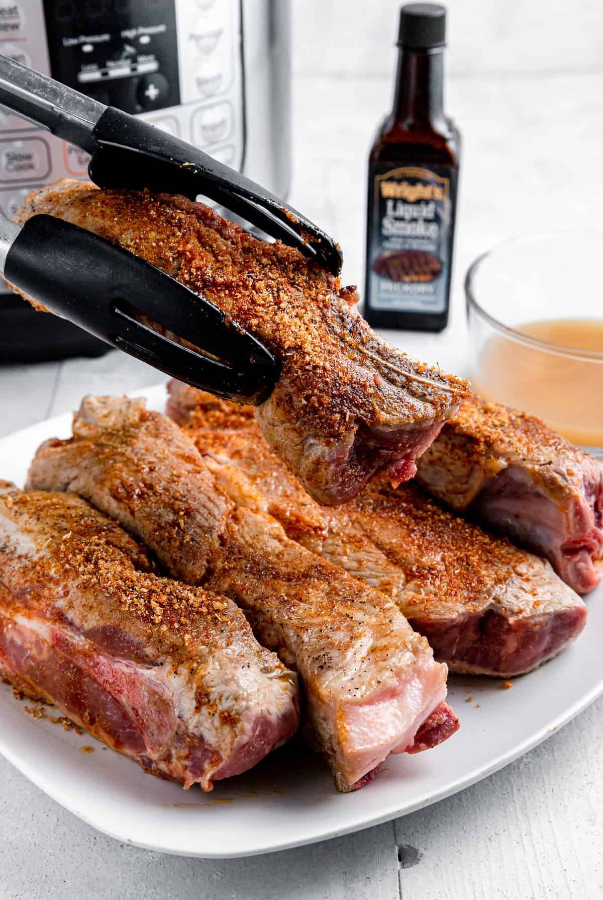 A Pair of Tongs Holding a Seasoned Pork Rib Over a Plate Full