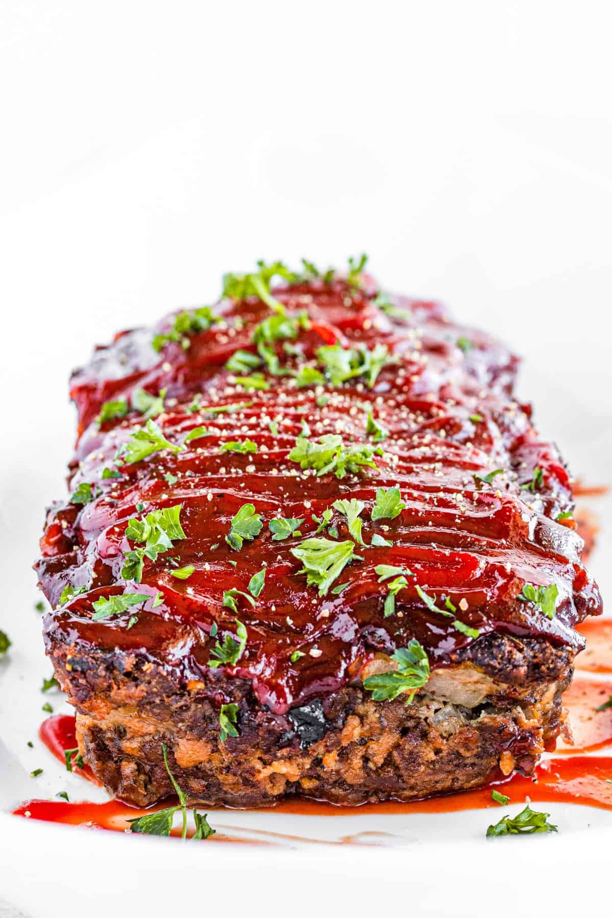 Cooked meatloaf topped with barbecue sauce and chopped fresh parsley.