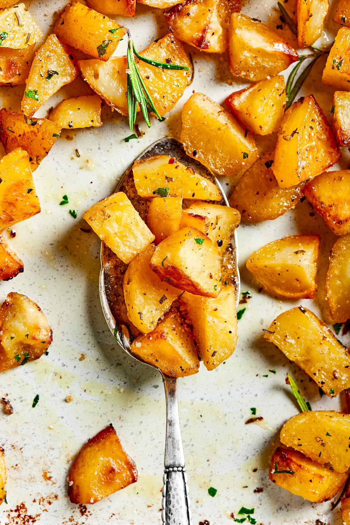 A tray of roast potatoes with a silver spoon lifting some of the potato pieces.