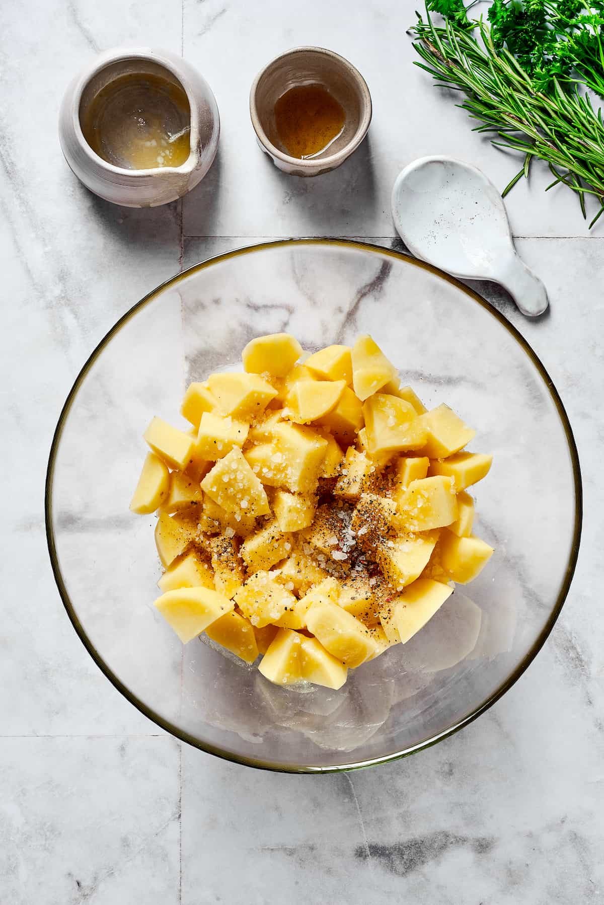 Raw potatoes and seasonings in a mixing bowl.