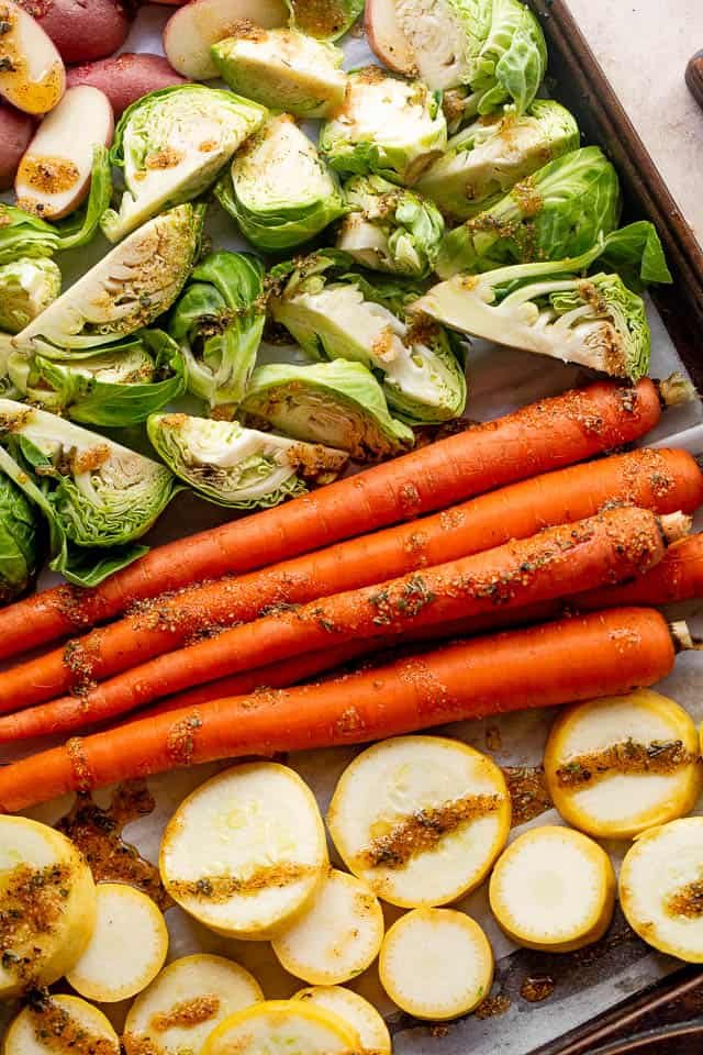 raw carrots, brussel sprouts, squash, and potatoes on a baking sheet