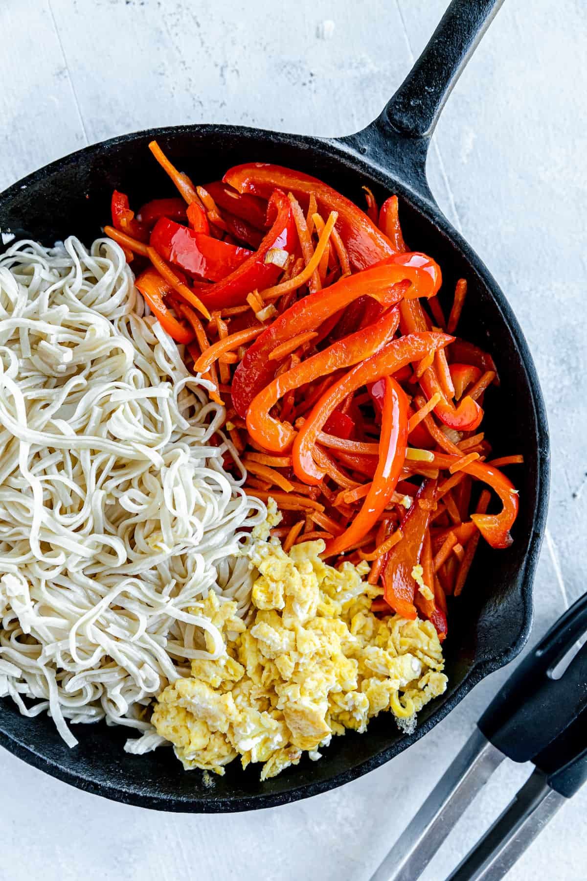 Scrambled Eggs, Brown Rice Noodles and Chopped Veggies Inside of a Black Skillet