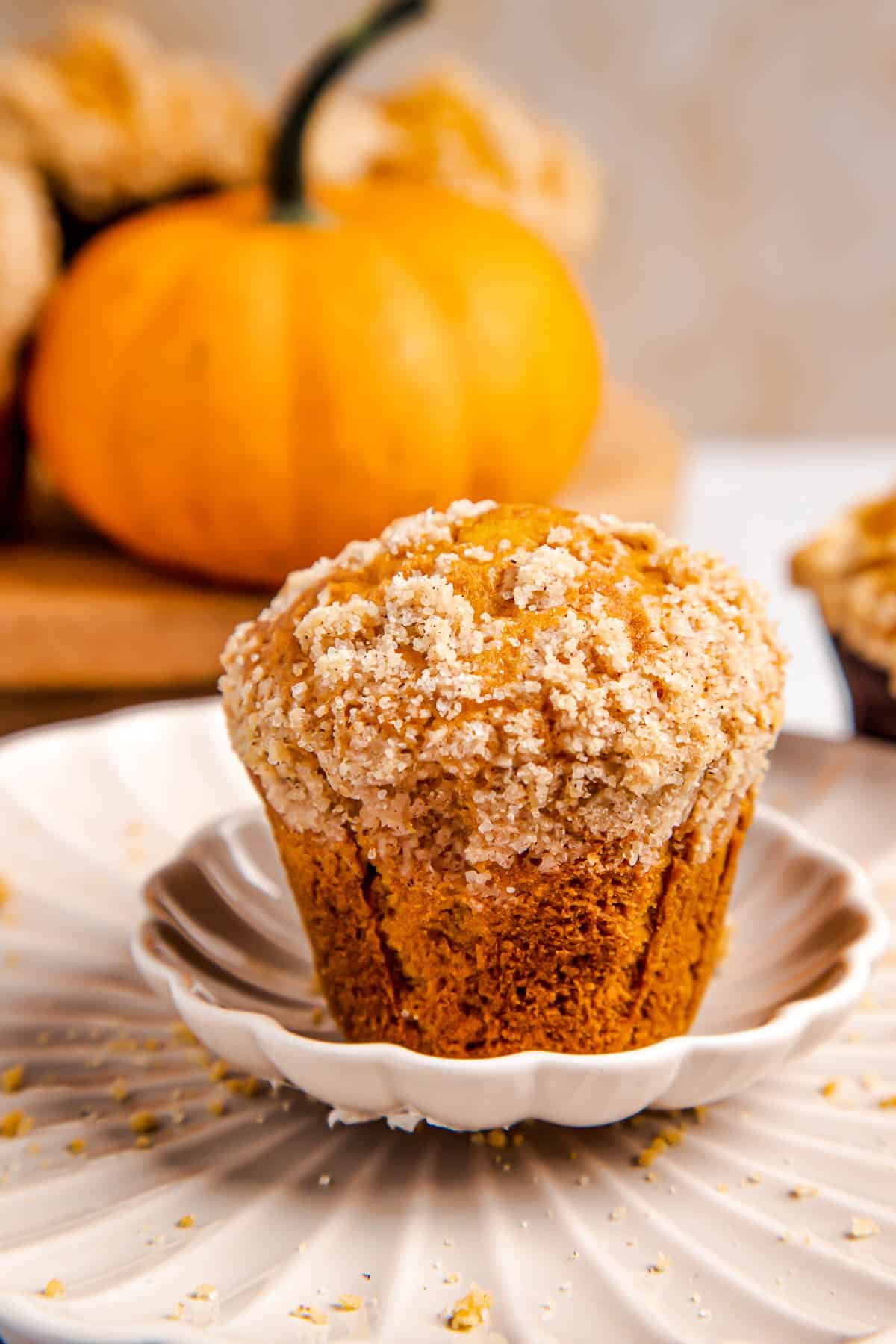 one pumpkin muffin on a white plate with three muffins behind it.