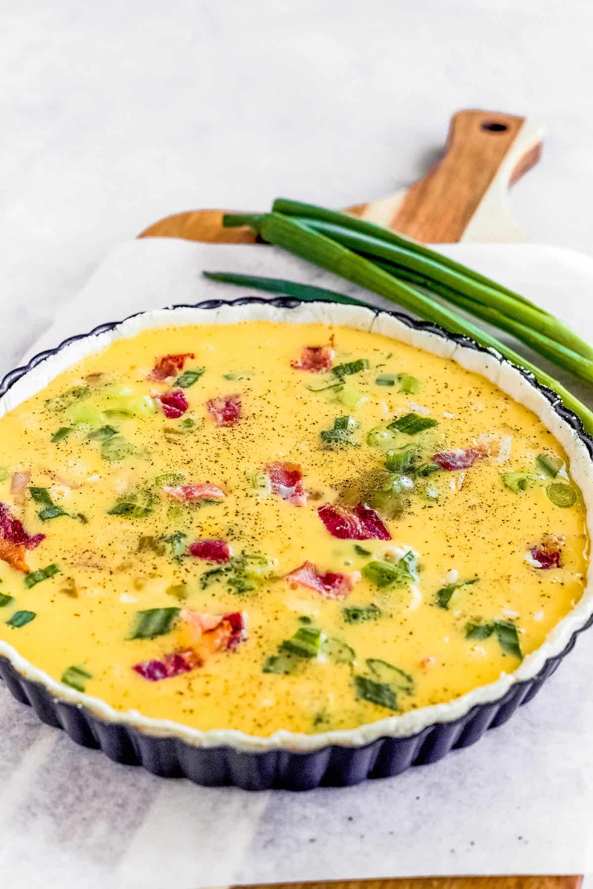 An Unbaked Quiche Lorraine on a Cutting Board Lined with Parchment Paper
