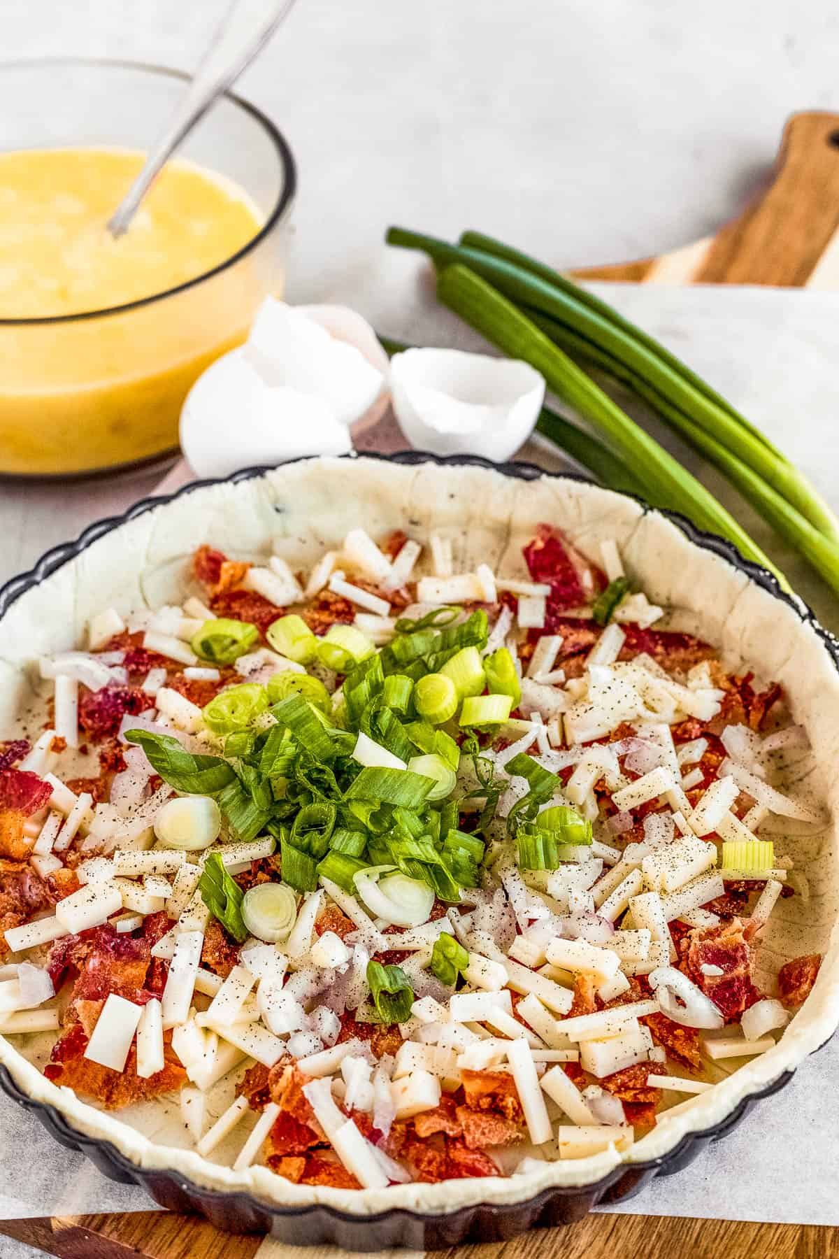 Chopped Onions, Shallots and Bacon Bits Inside of a Pie Crust with the Egg Mixture in the Background