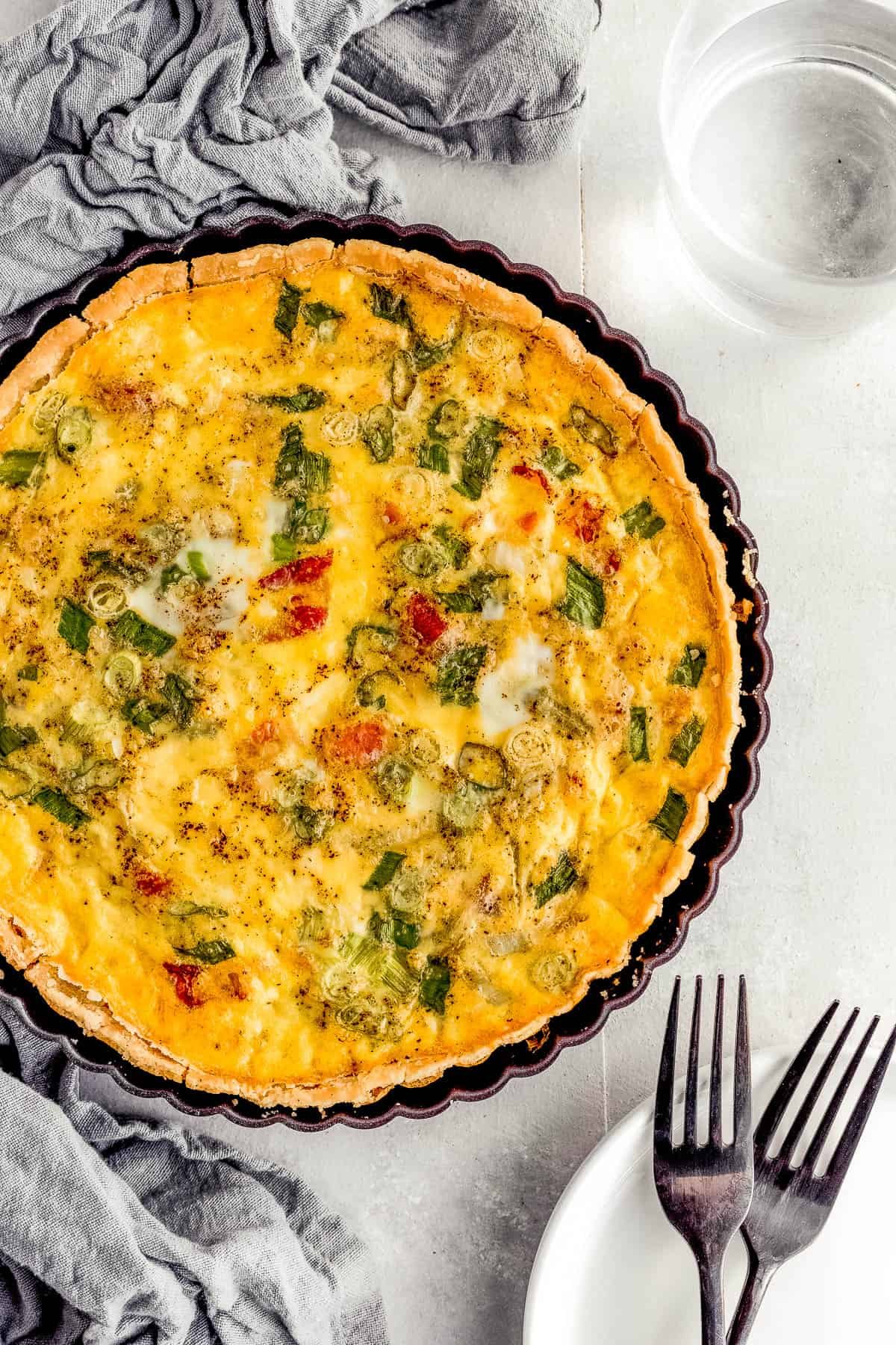 A Bacon Quiche Lorraine Beside a Gray Tablecloth and a Glass of Water