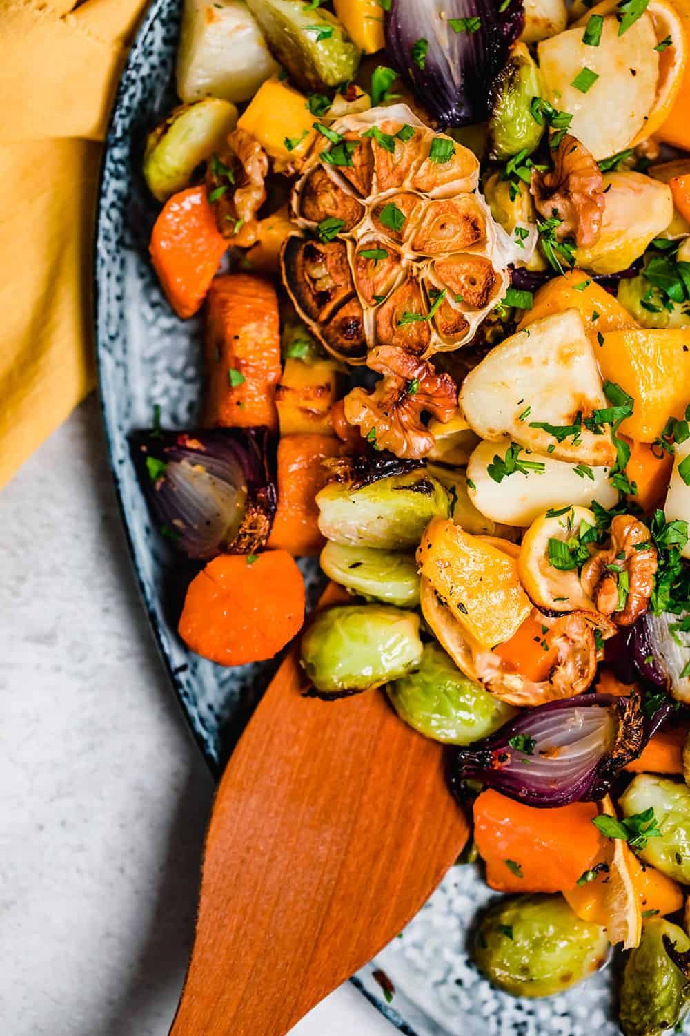 A wooden spoon resting on roasted vegetables on a blue platter.