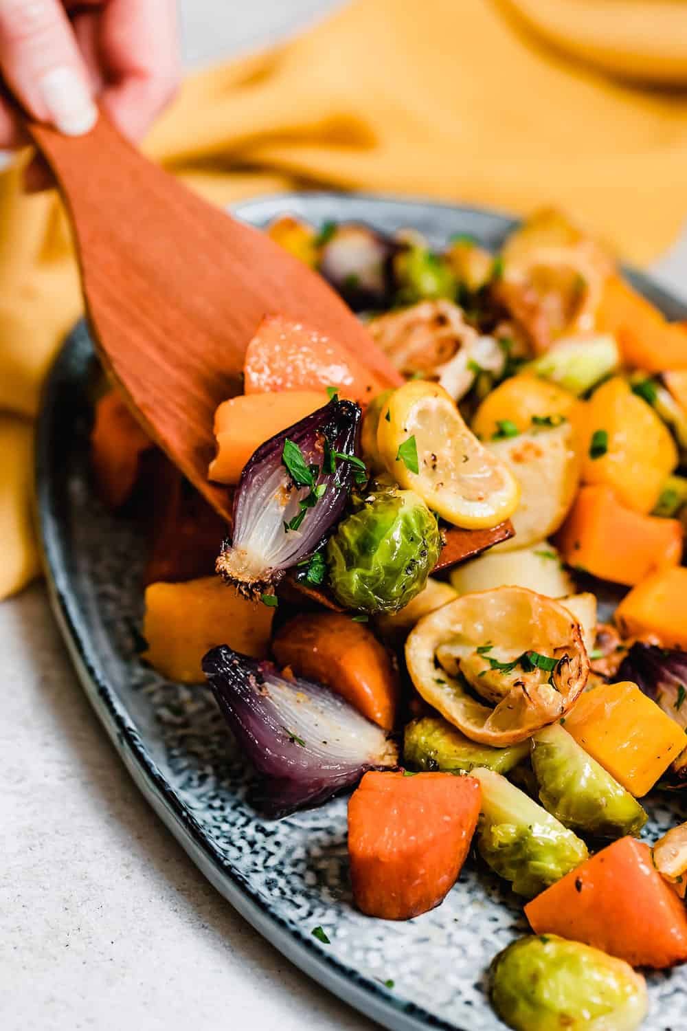 A wooden spoon scooping roasted vegetables off a blue platter.
