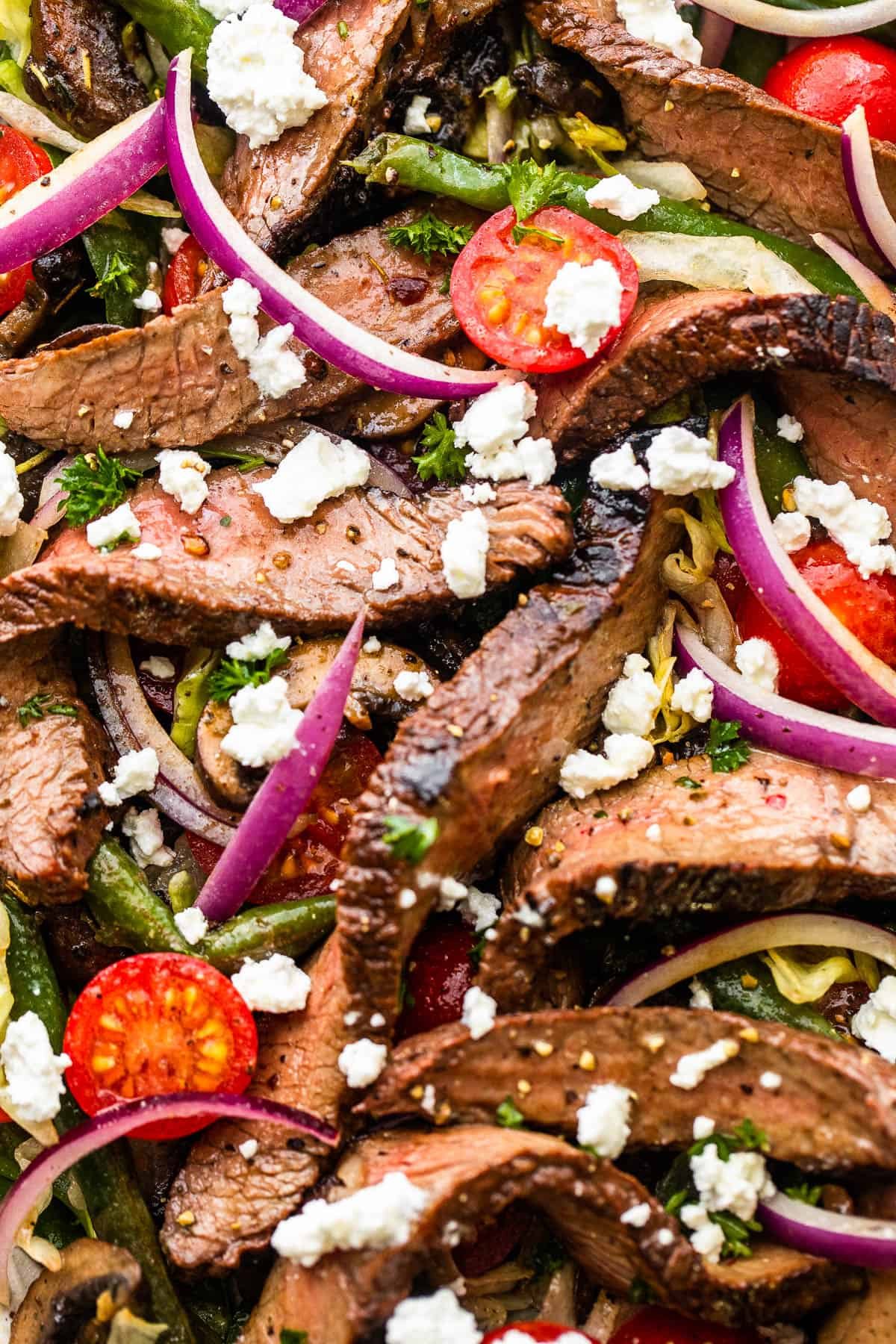 up close photo of Steak Salad on a long plate topped with cheese crumbles, tomatoes, and mushrooms