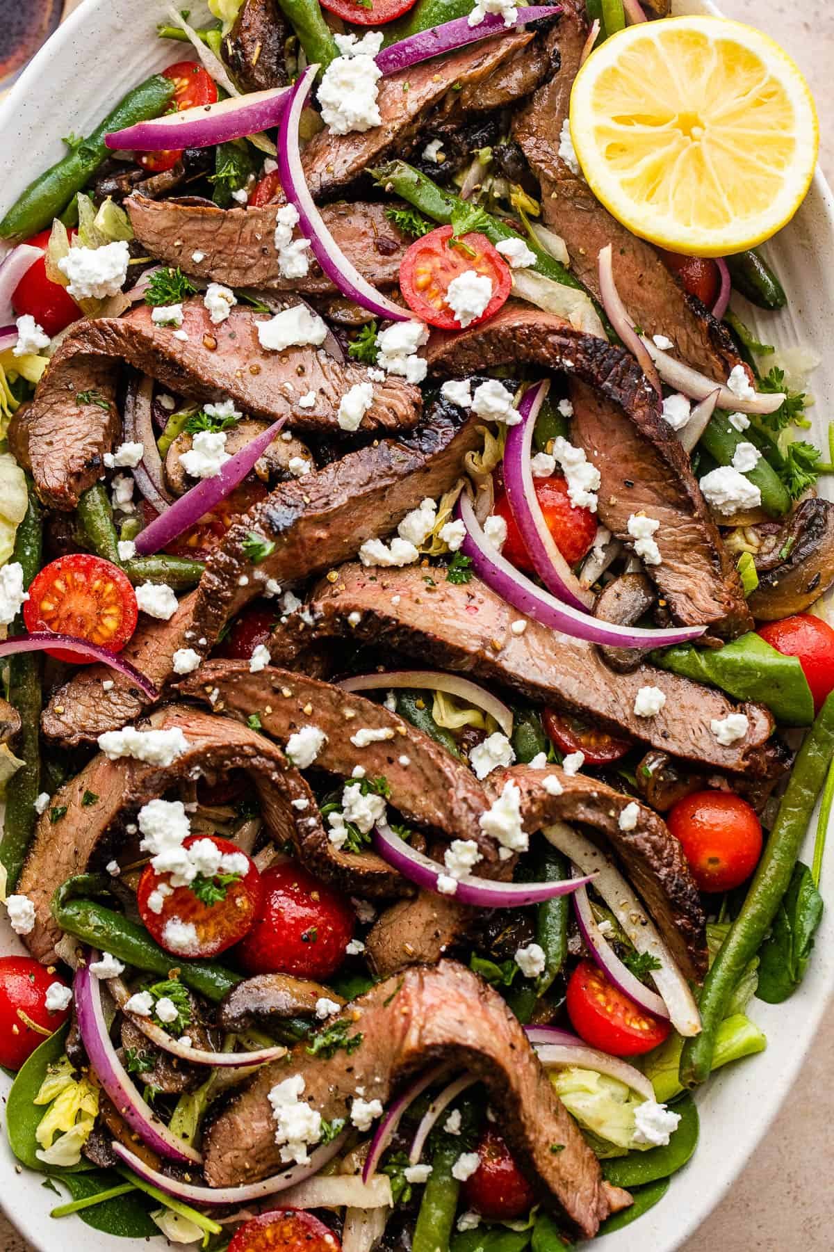 Steak Salad served on a long plate topped with cheese crumbles, tomatoes, and mushrooms