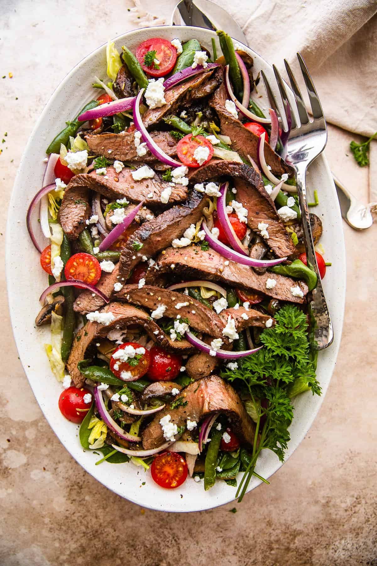 Steak Salad on a long plate topped with cheese crumbles, tomatoes, and mushrooms