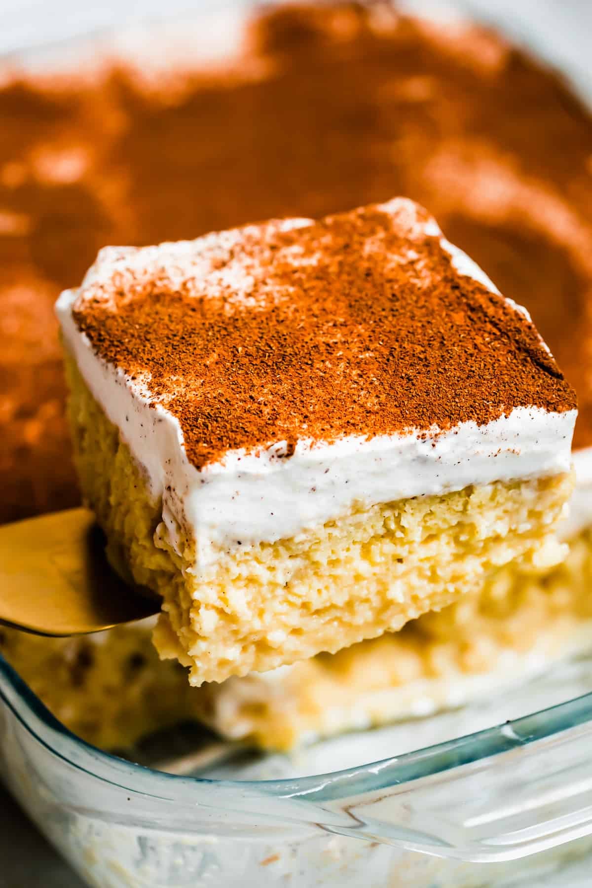 Lifting out a piece of tres leches cake from a glass baking dish.