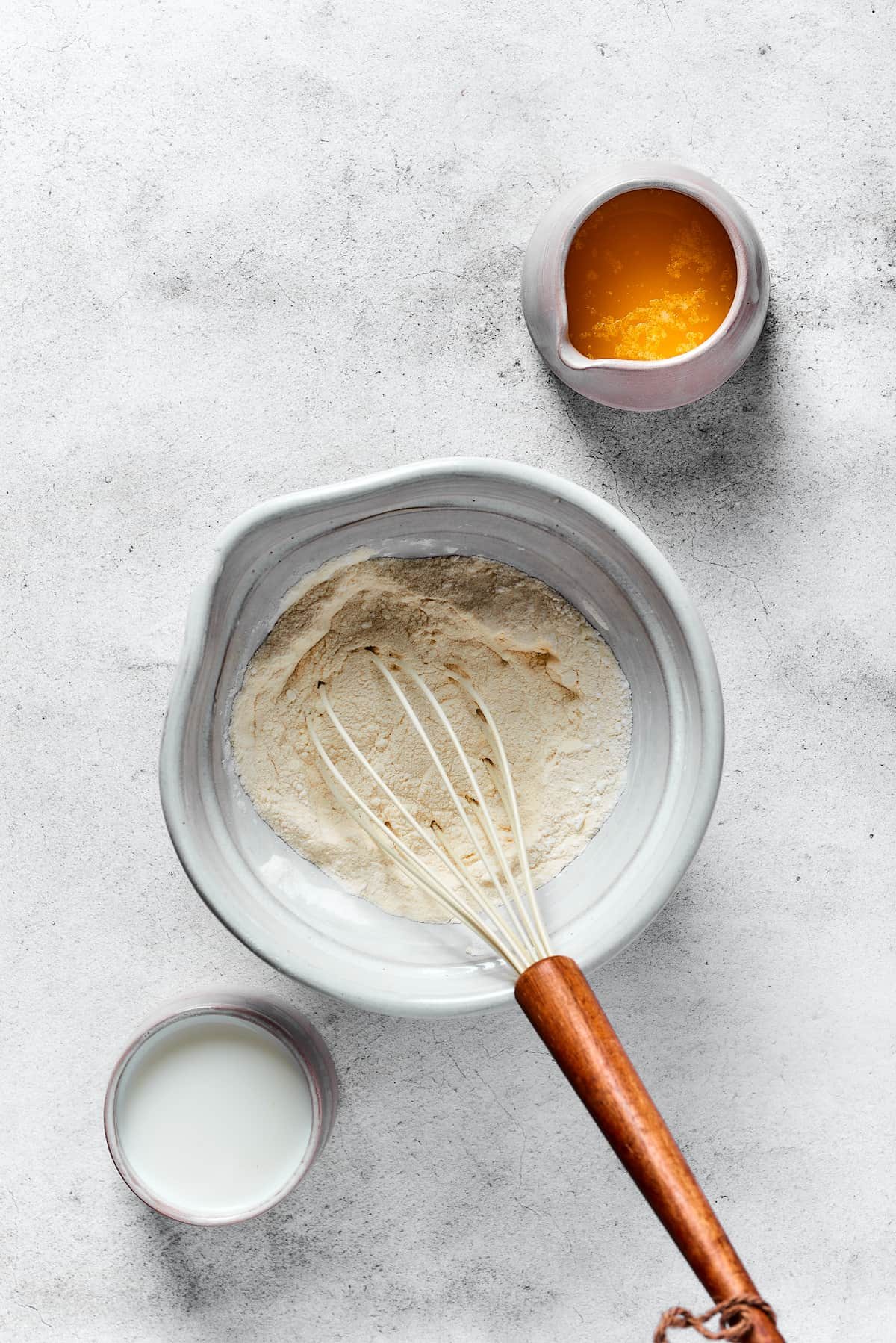 A small pitcher of melted butter, and a cup of buttermilk, next to a mixing bowl of waffle batter ingredients.