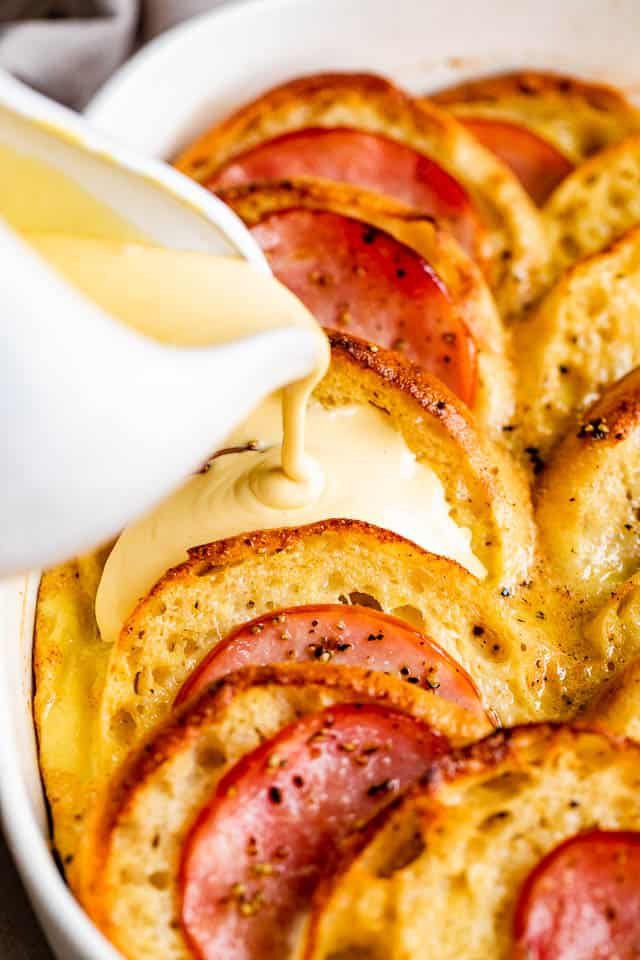 pouring hollandaise sauce over eggs benedict casserole