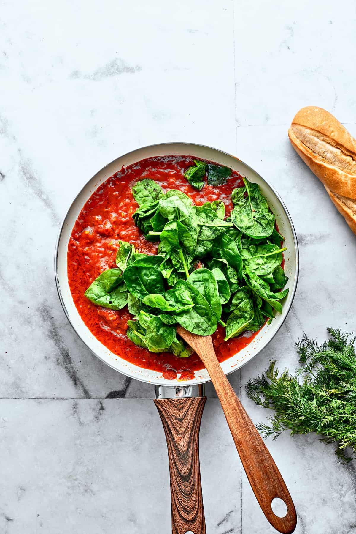 Bright green spinach leaves are stirred into a skillet of homemade tomato sauce.