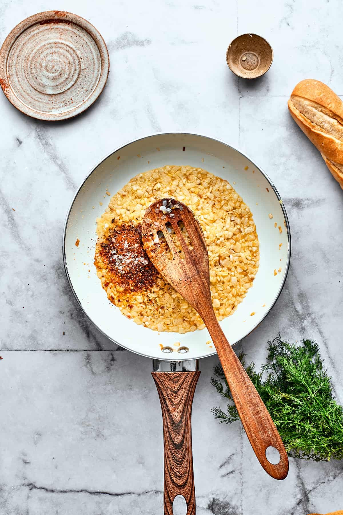 A wooden spoon stirs diced tomatoes into a skillet of onion and garlic.