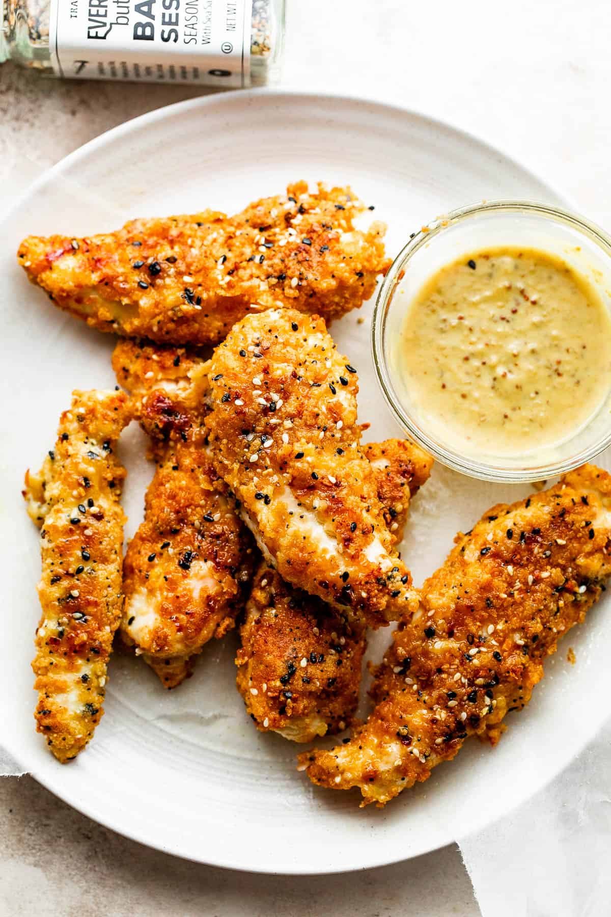 Everything Bagel Chicken Tenders arranged on a round plate and served with honey mustard dipping sauce