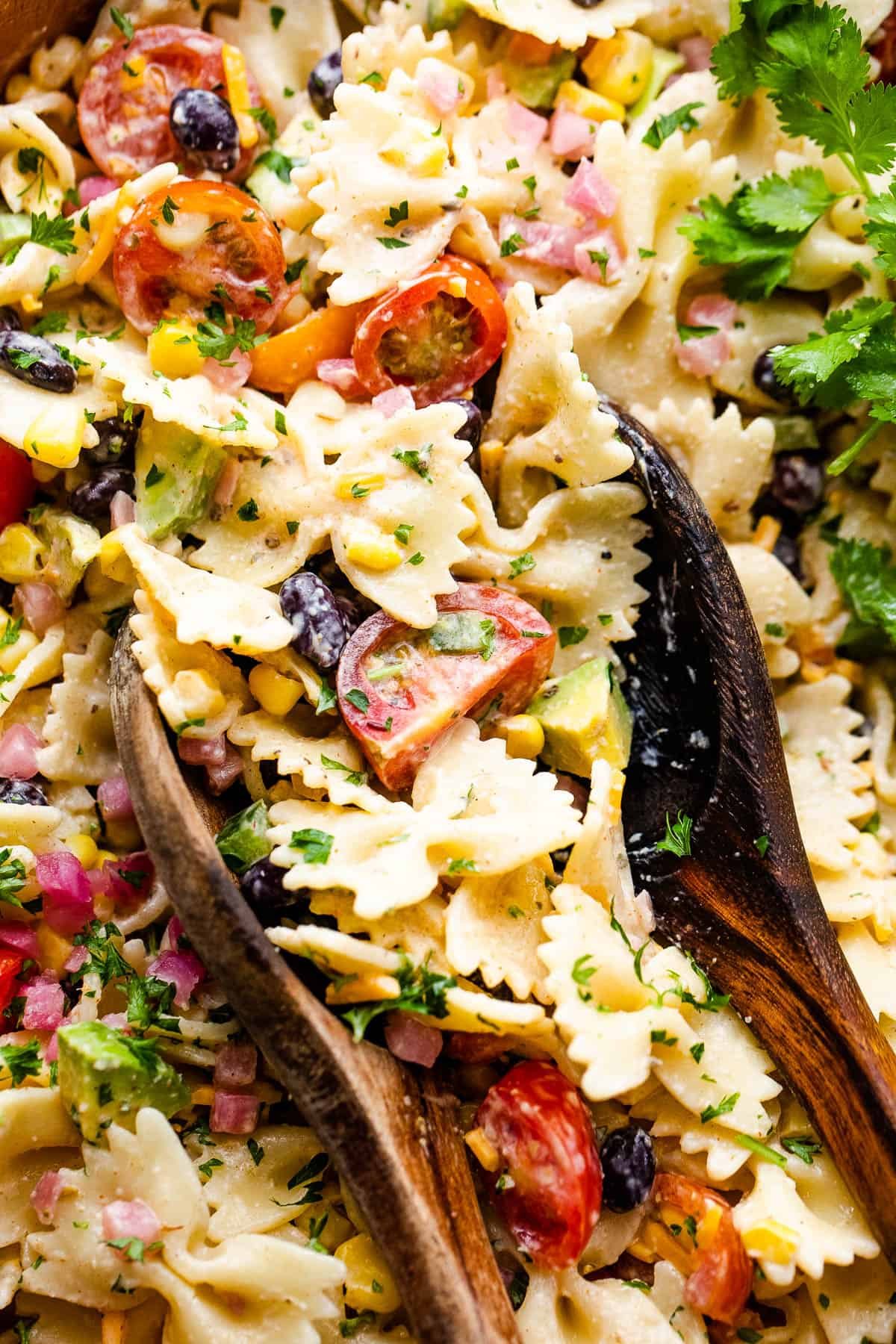 up close shot of fiesta pasta salad in a wooden salad bowl with two wooden spoons