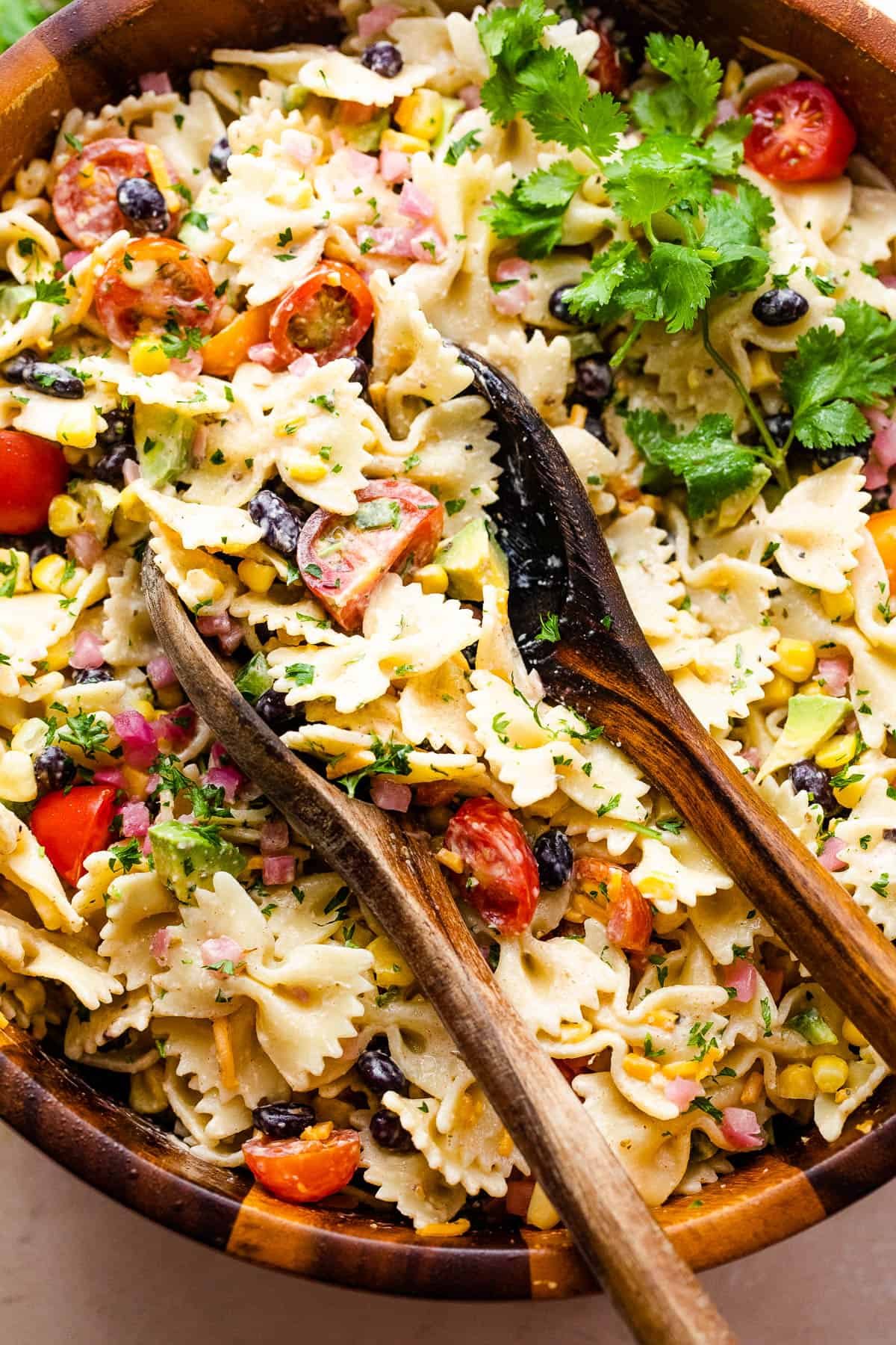 pasta salad in a wooden salad bowl with two wooden spoons