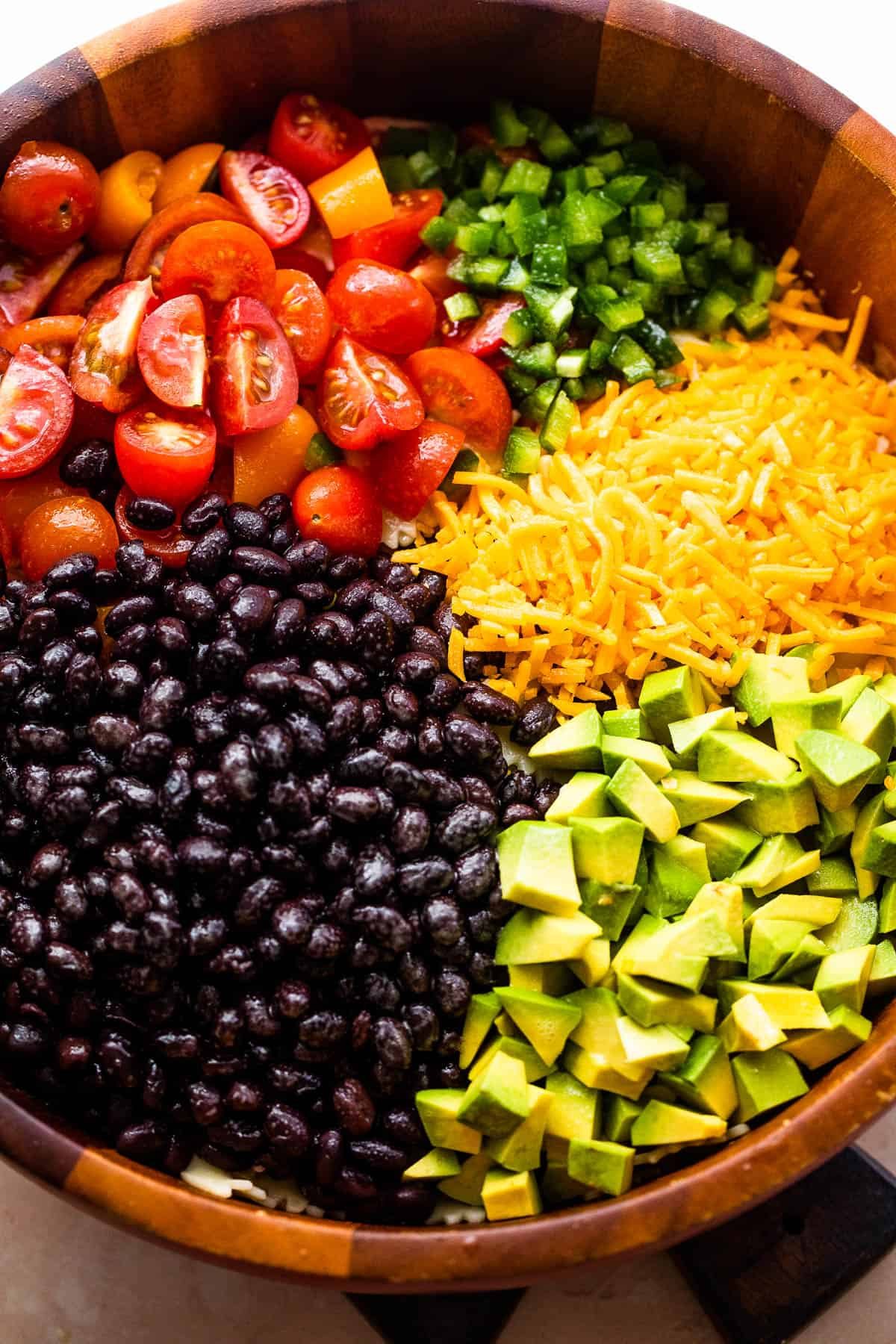 wooden bowl with chopped up tomatoes, avocado, shredded cheese, and black beans