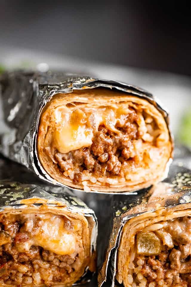 close up shot of three cheesy beef burritos cut in half