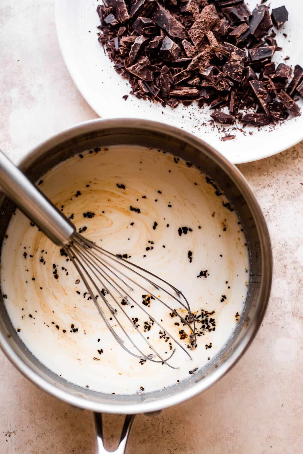overhead shot of a saucepan filled with heavy cream and a plate with chopped chocolate placed nearby.
