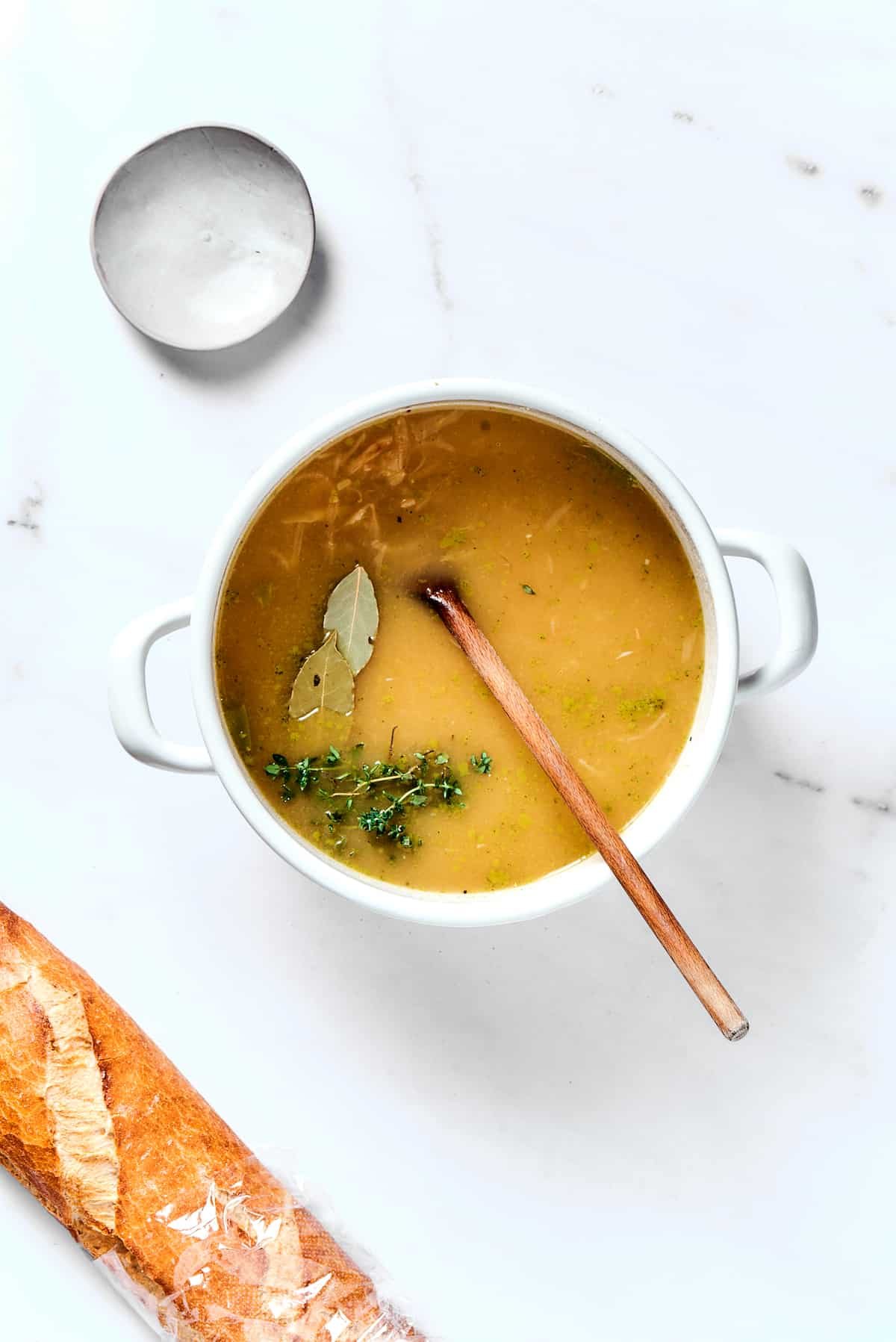 French onion soup cooking in a heavy pot with bay leaves and thyme sprigs.