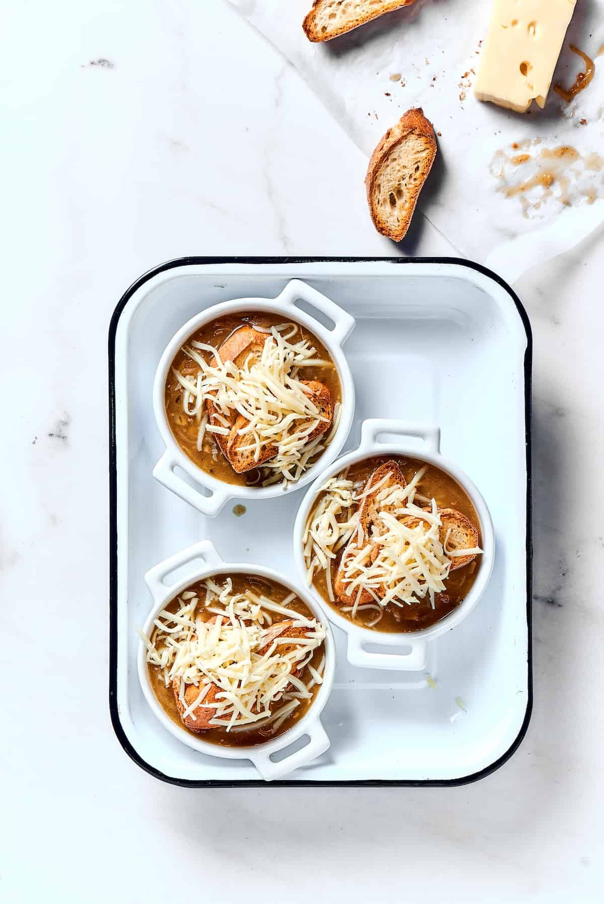 Individual bowls of soup topped with toasted baguette and shredded cheese.