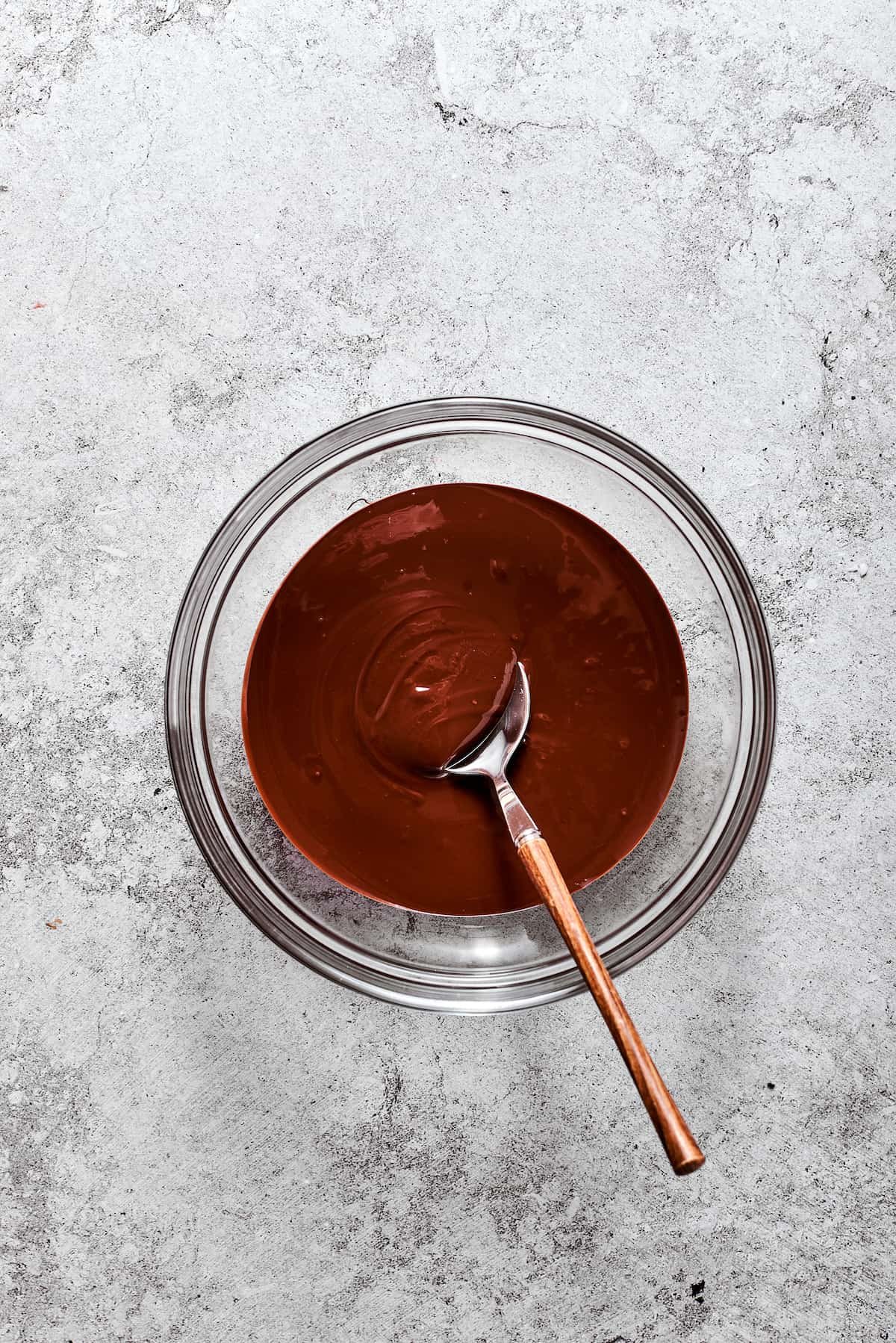 Melted chocolate in a glass bowl with a wooden spoon.